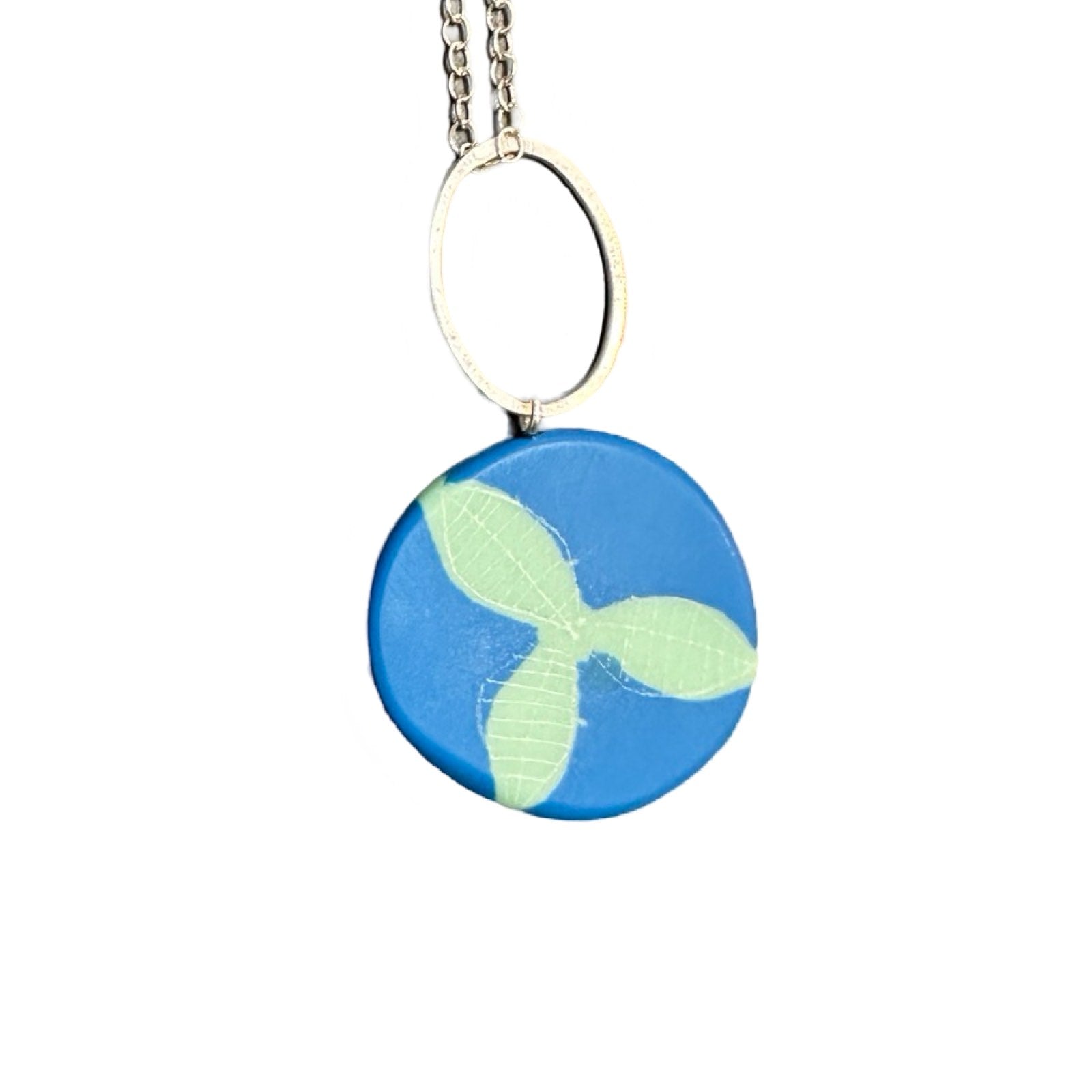 A blue pendant necklace made from resin with green leaves in the centre on a silver chain.