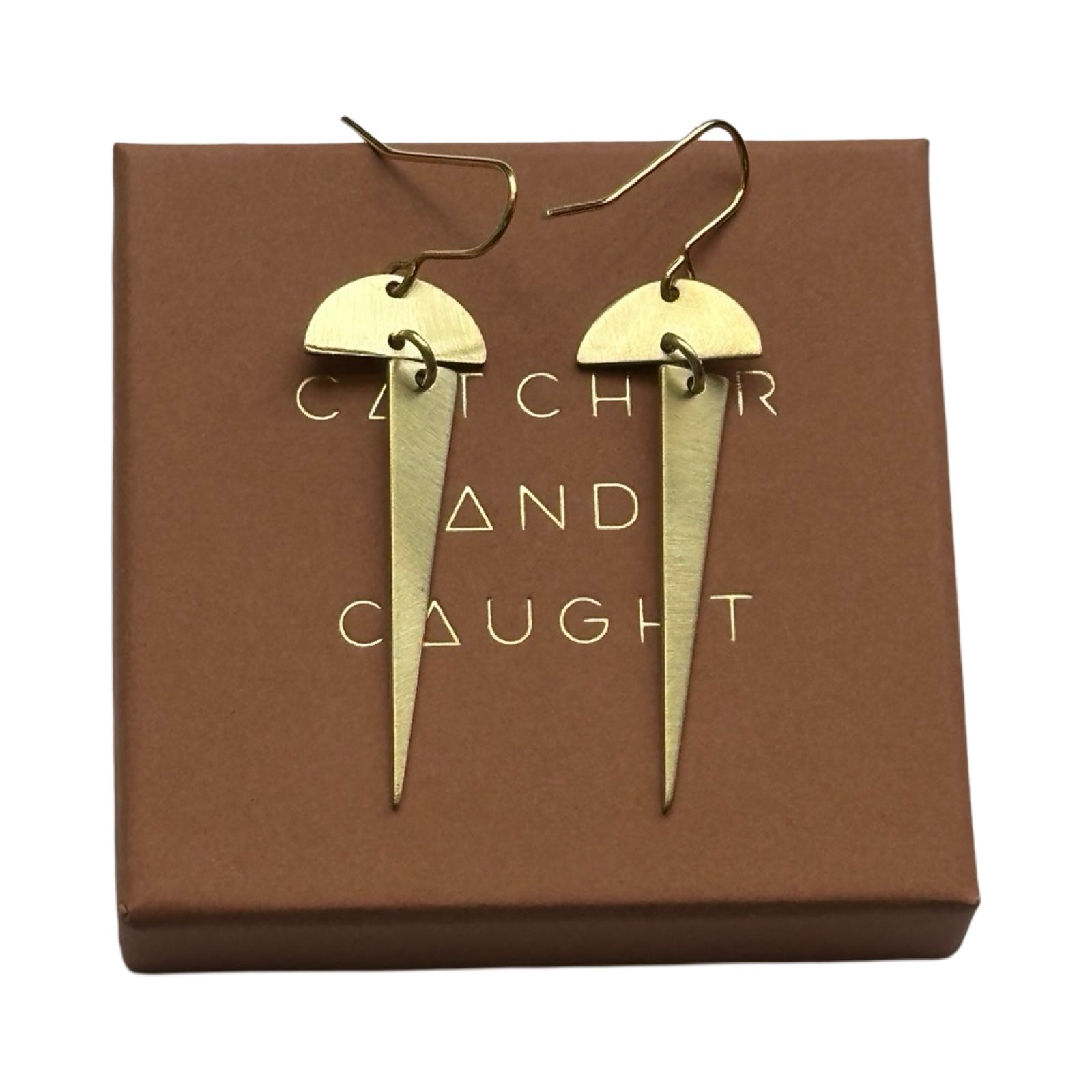 Brass earrings in geometric shapes, an arc with a long triangle hanging below on top of a brown branded gift box.