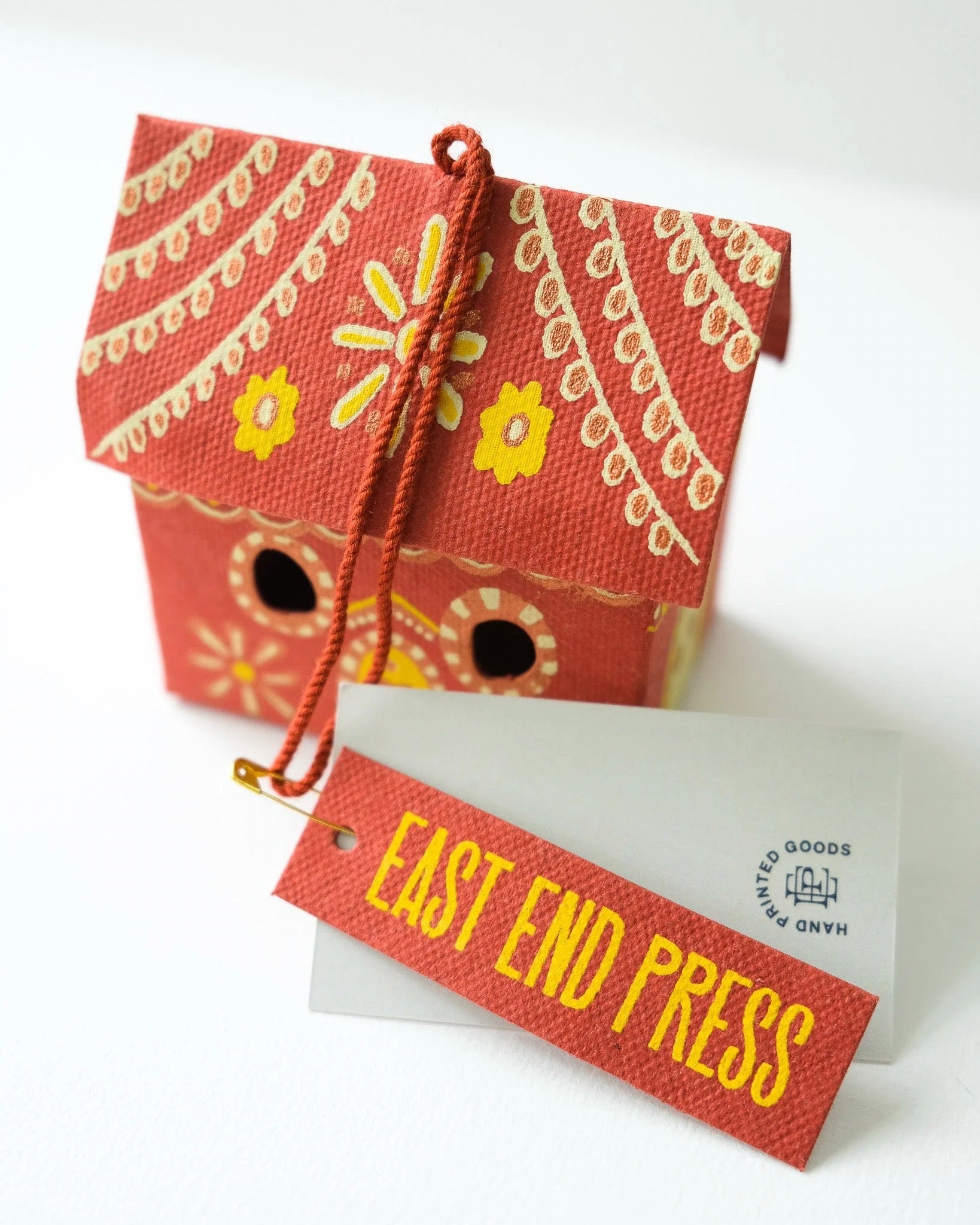 Decorative red house with yellow floral patterns and a 'East End Press' tag on a white background.