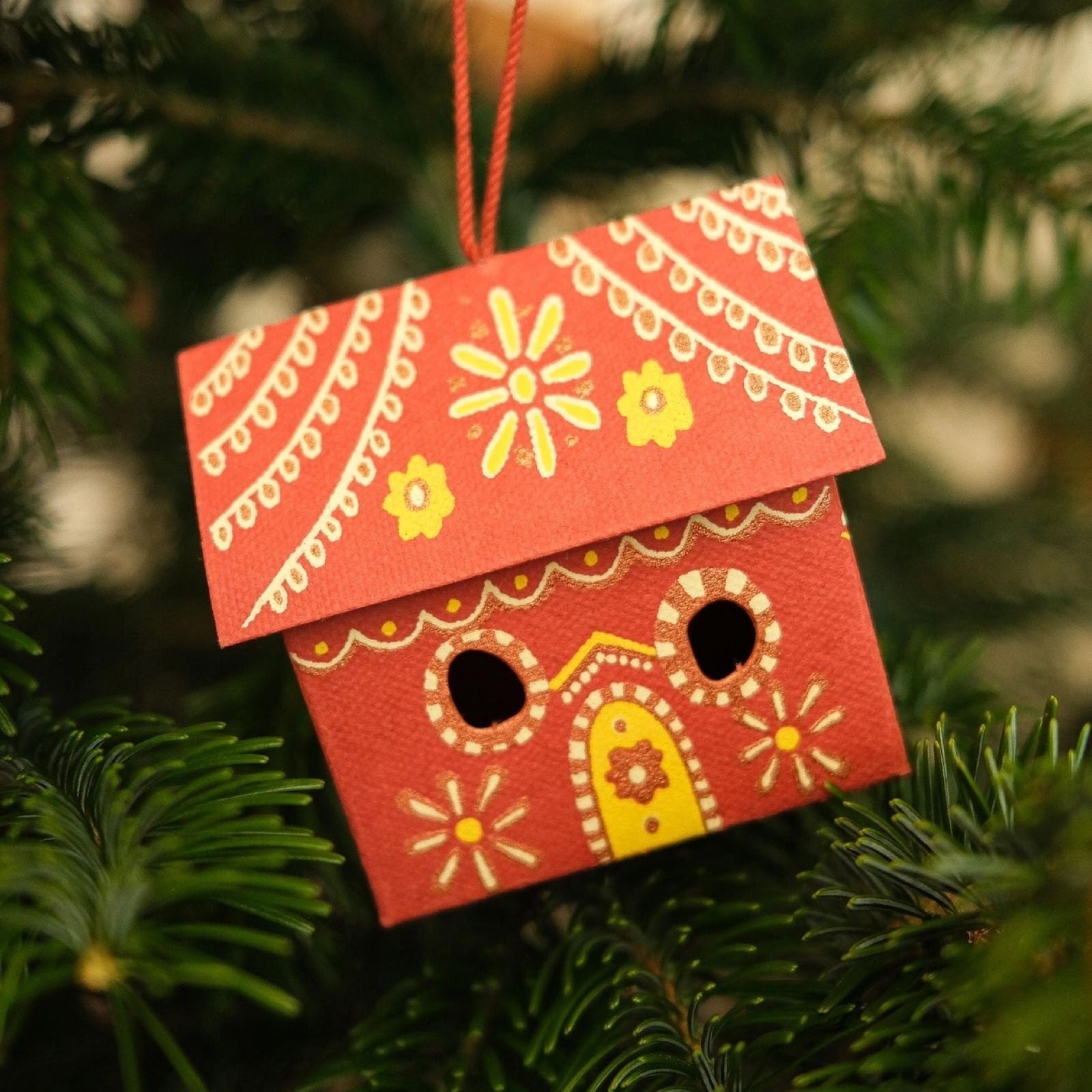 A red and gold gingerbread house three-dimensional decoration hanging on a Christmas tree.