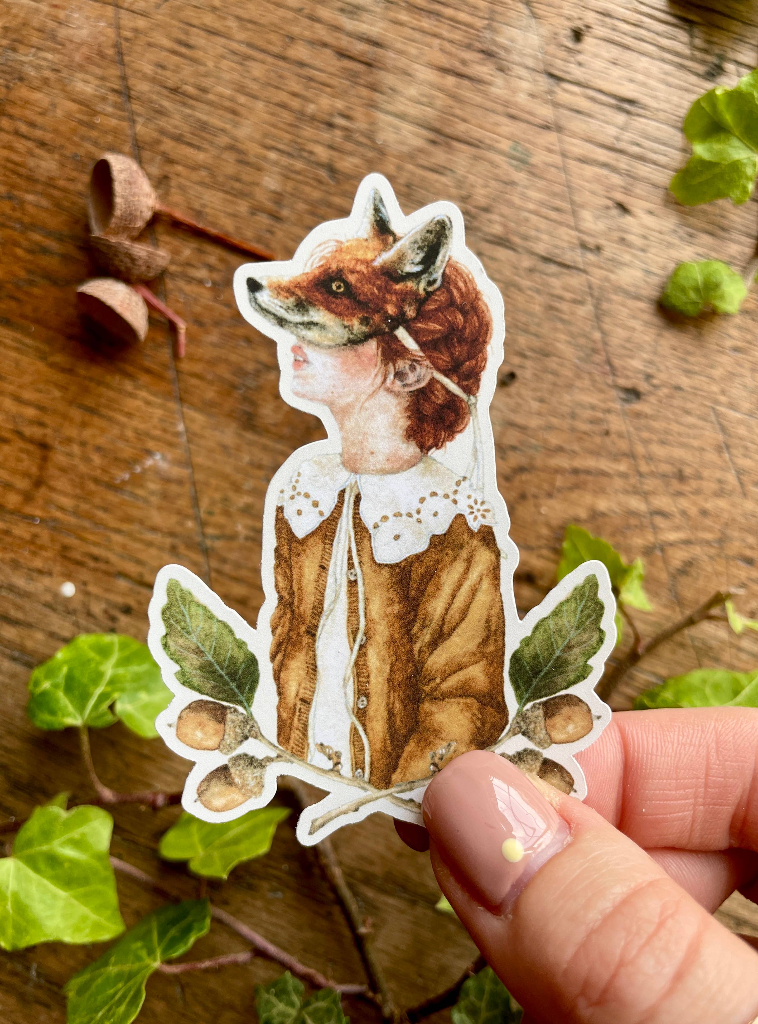 A vinyl watercolour sticker of a girl wearing a fox mask, dressed in a white shirt with a fabulous lace collar and a brown coat, and surrounded by leaves and acorns.