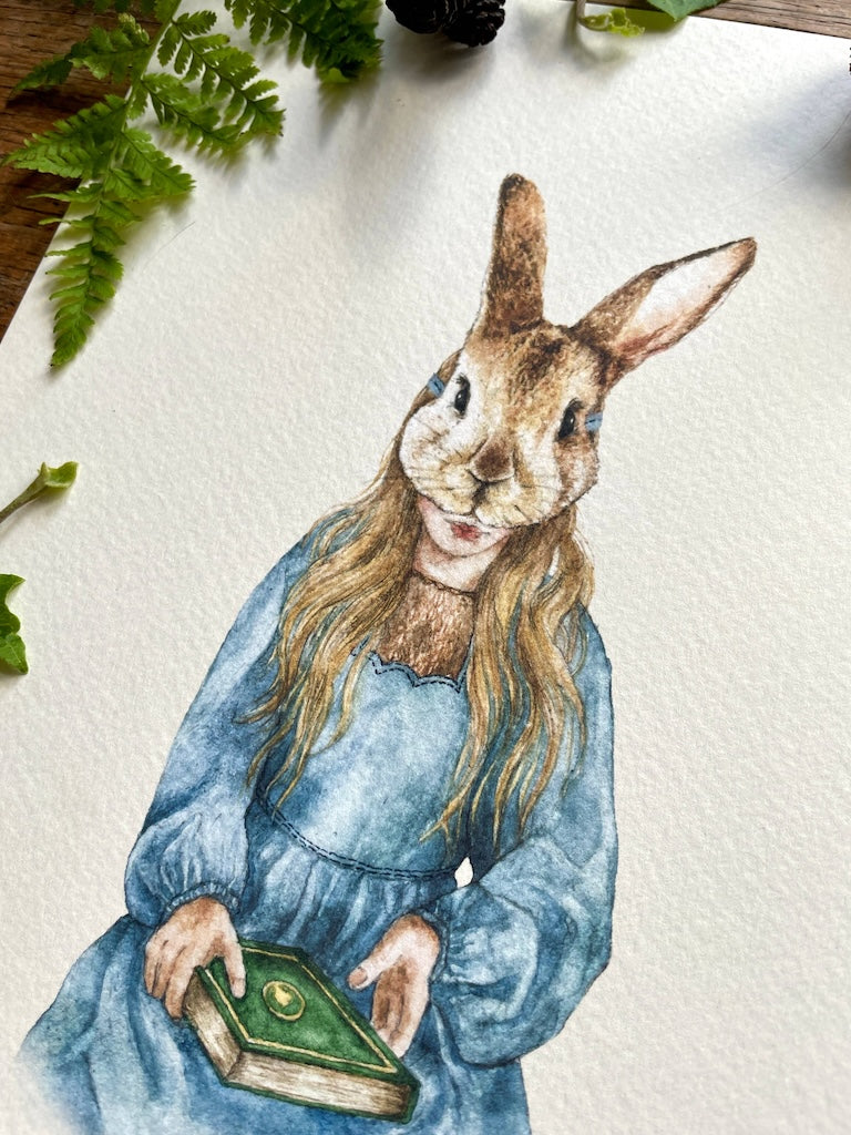 Framed artwork of a rabbit character in a blue dress holding a book on a textured white background