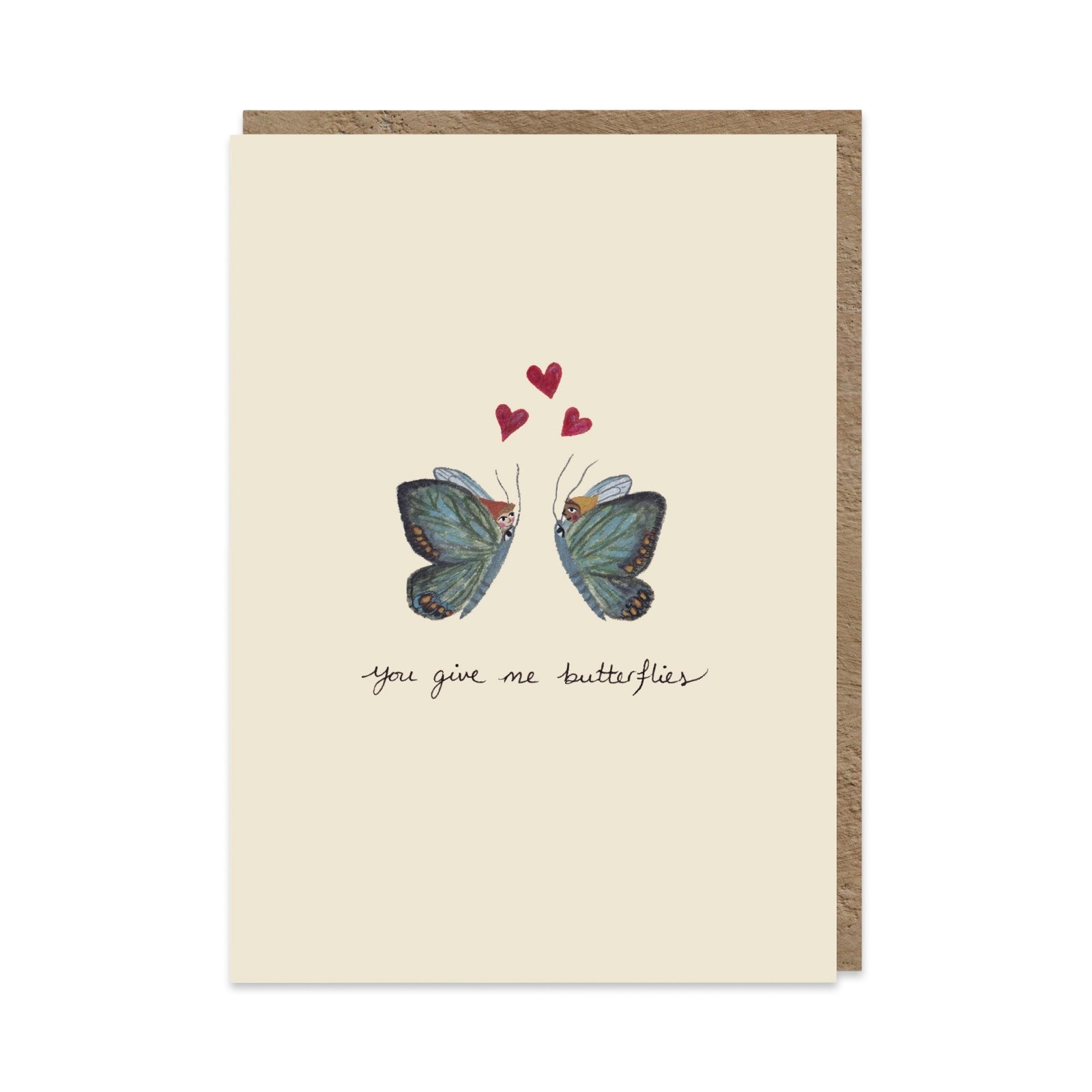 A cream greeting card with a brown envelope behind it, featuring an illustration of two blue butterflies facing each other with three small red hearts above them and the handwritten text 'you give me butterflies' below.