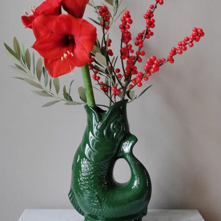 Green fish-shaped jug with red flowers and berries on a plain background.