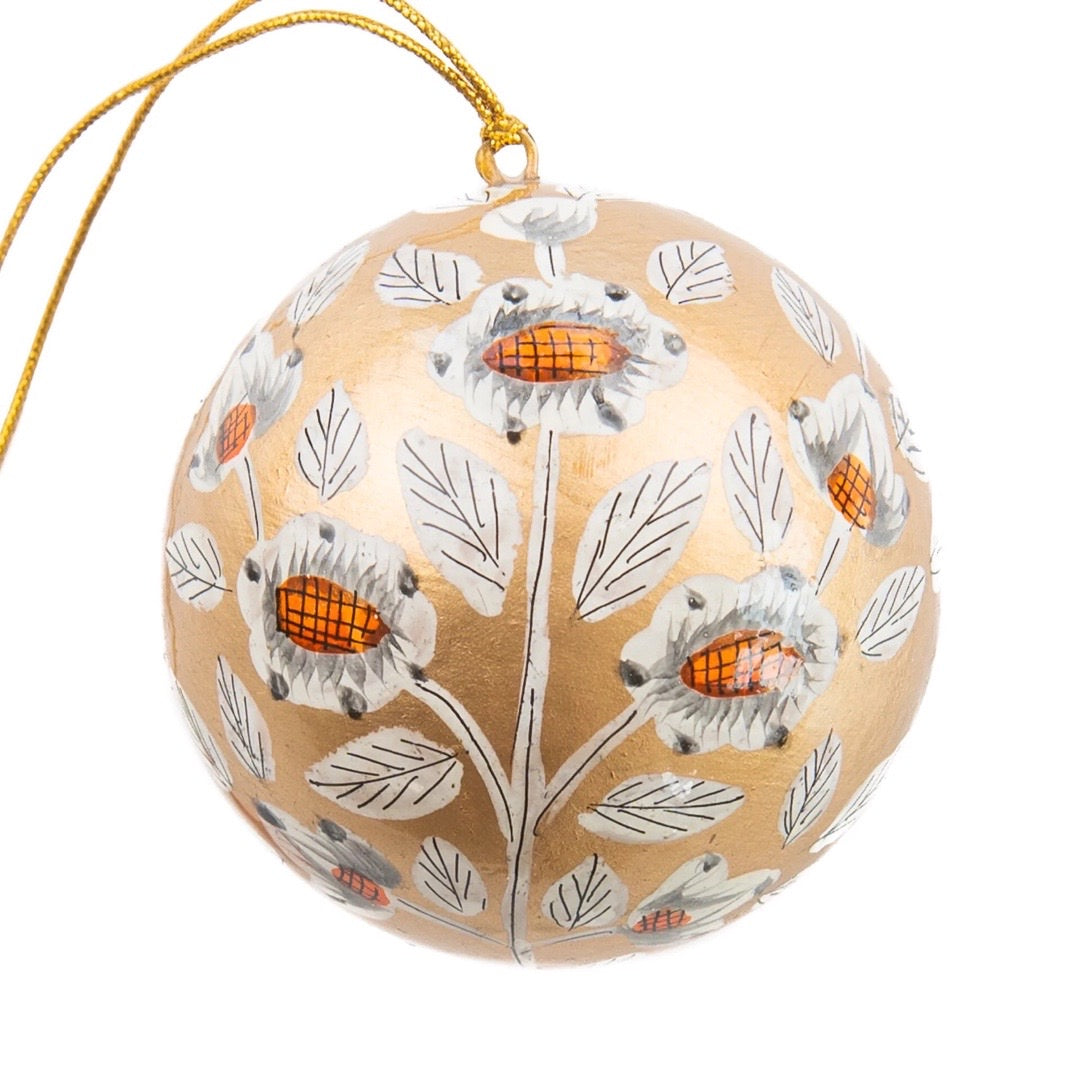 A round papier mache bauble in gold with a white, black and orange floral design.