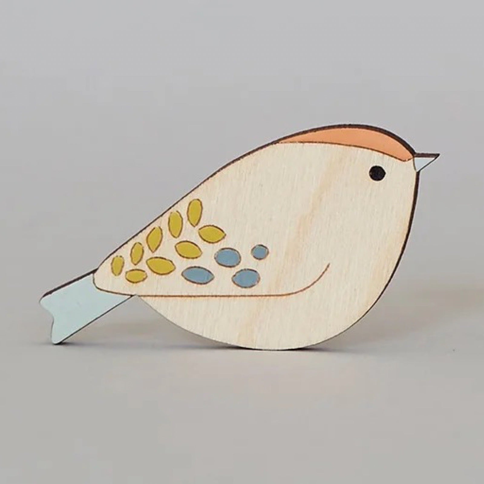 Wooden bird brooch with colourful design on a grey background.