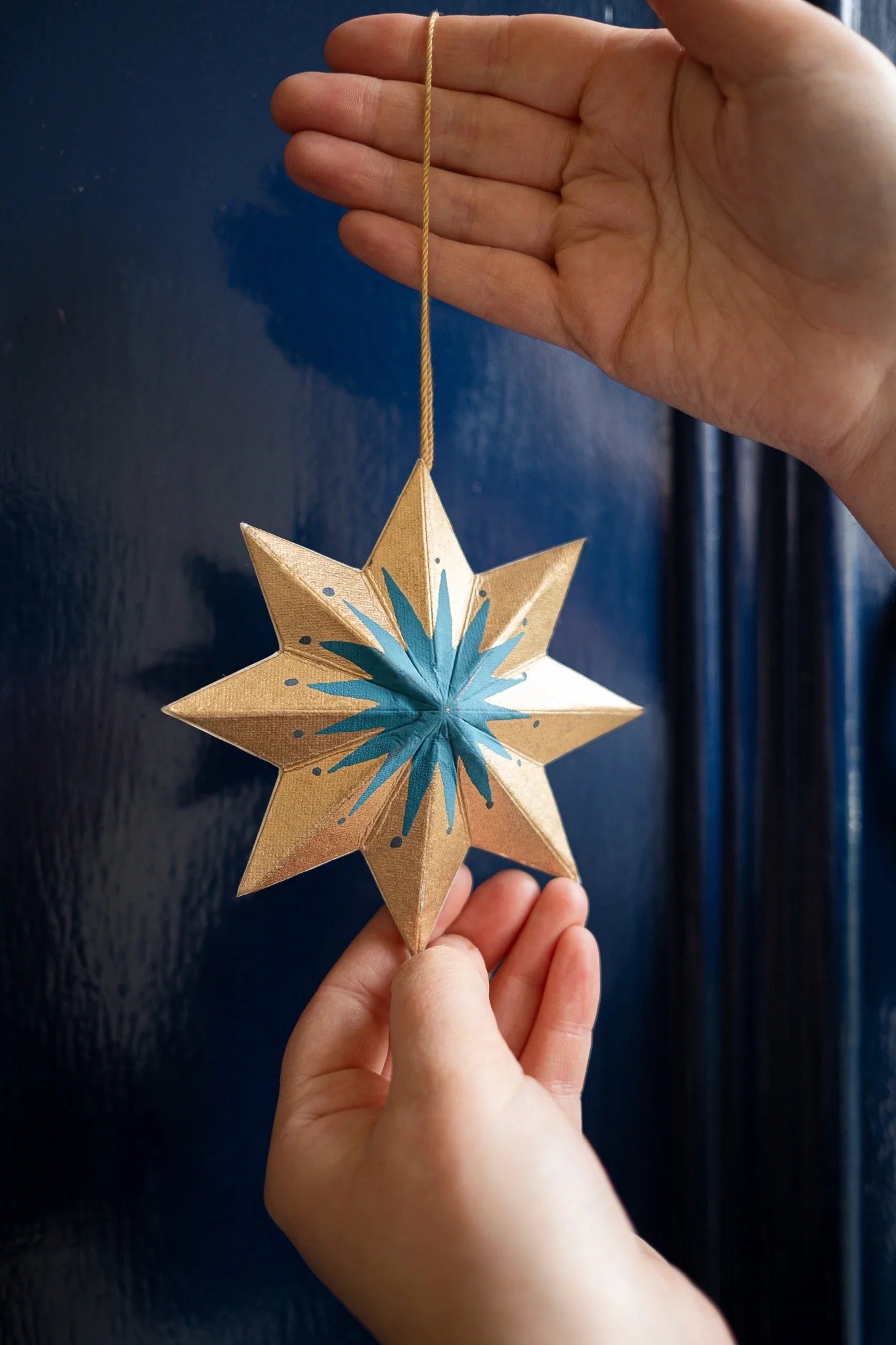 Hand holding a star-shaped ornament with blue centre against a dark background.