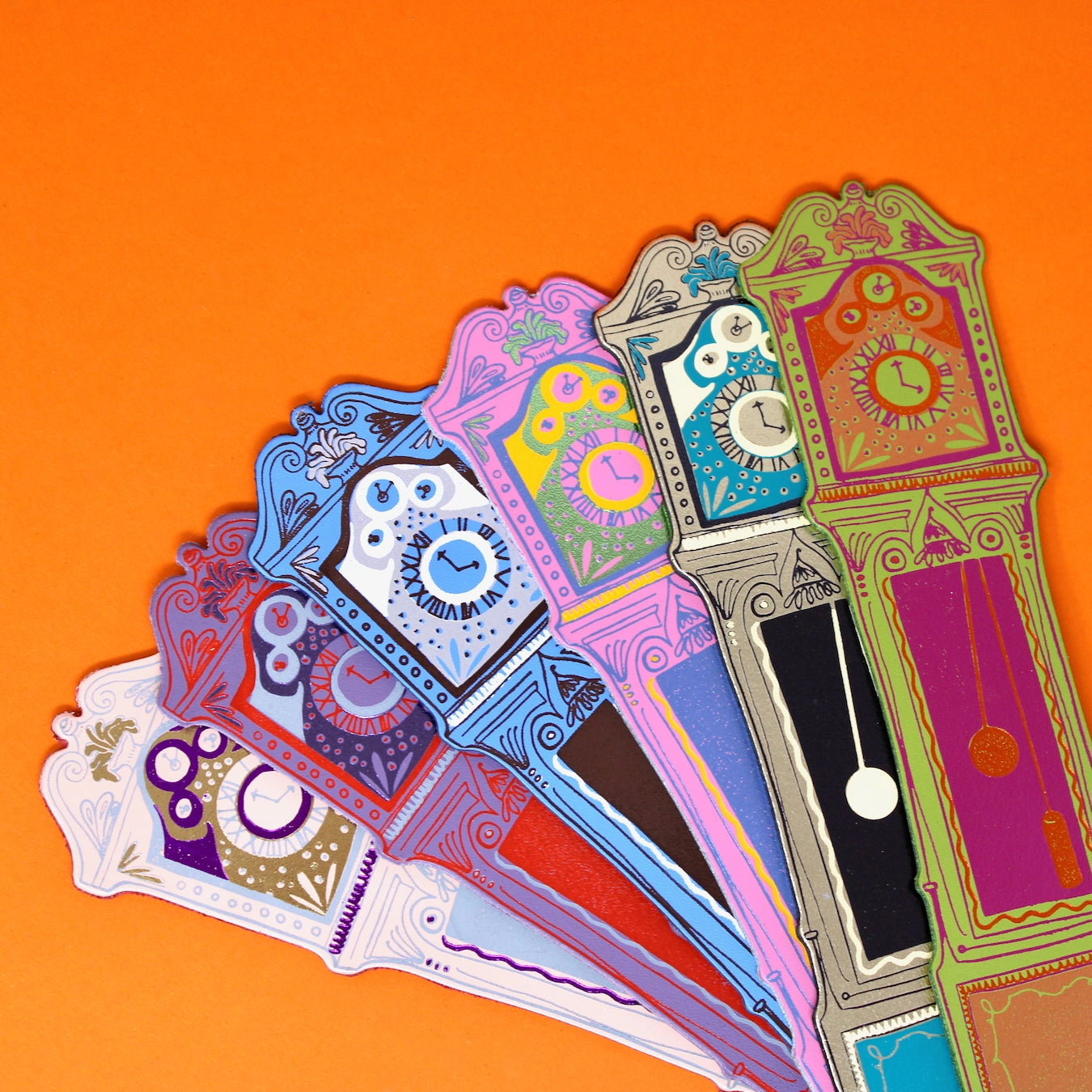 Colourful decorative grandfather clock bookmarks on an orange background.