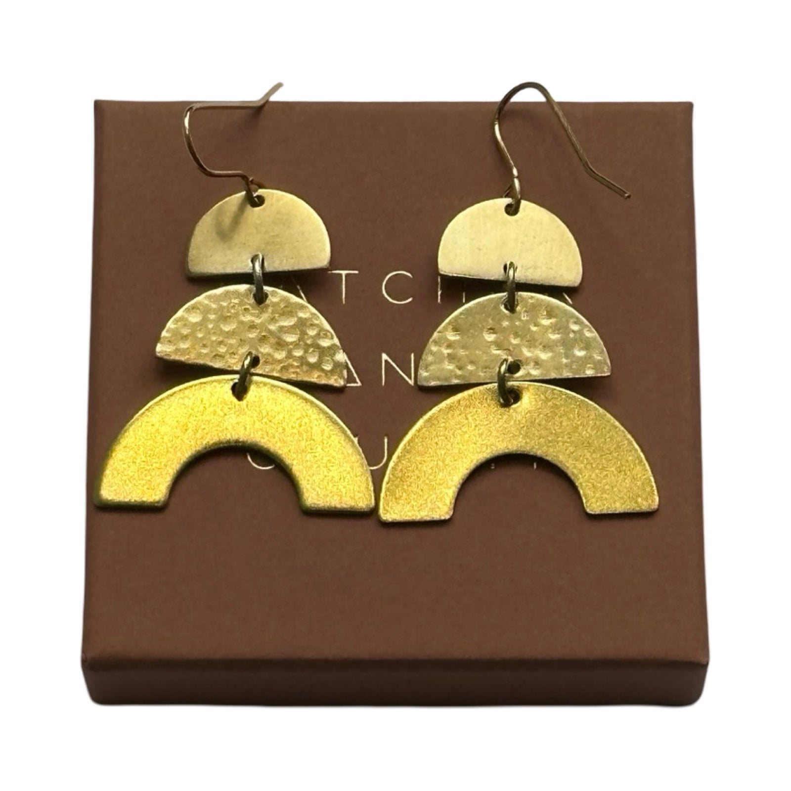 Brass dangle earrings in geometric shapes, a matt finish semi circle on the top, a hammered semi circle below and an arc at the bottom with gold-plated ear hooks, on a brown branded gift box.