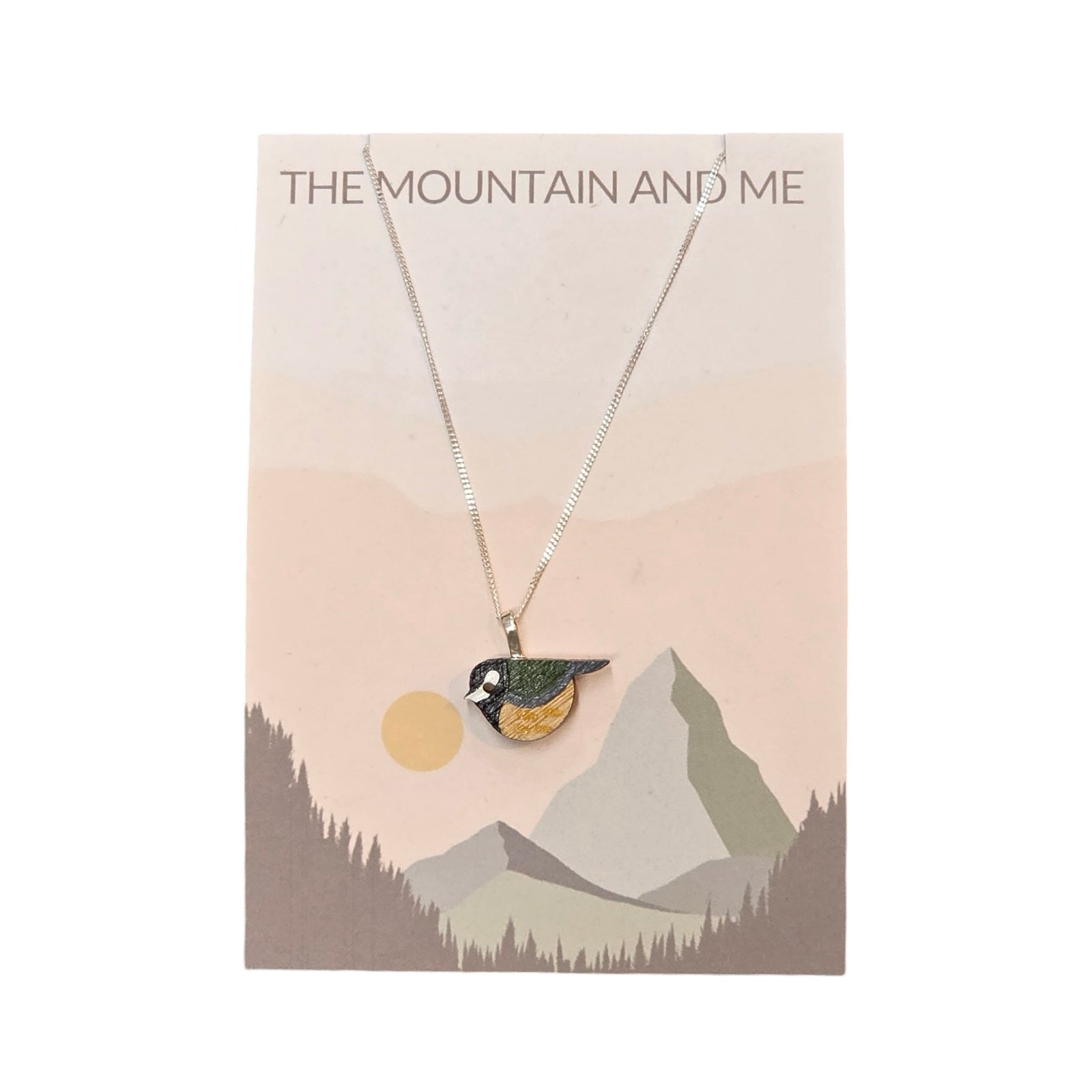 A green and black great tit bird-shaped painted pendant with a sterling silver chain on a branded backing card.