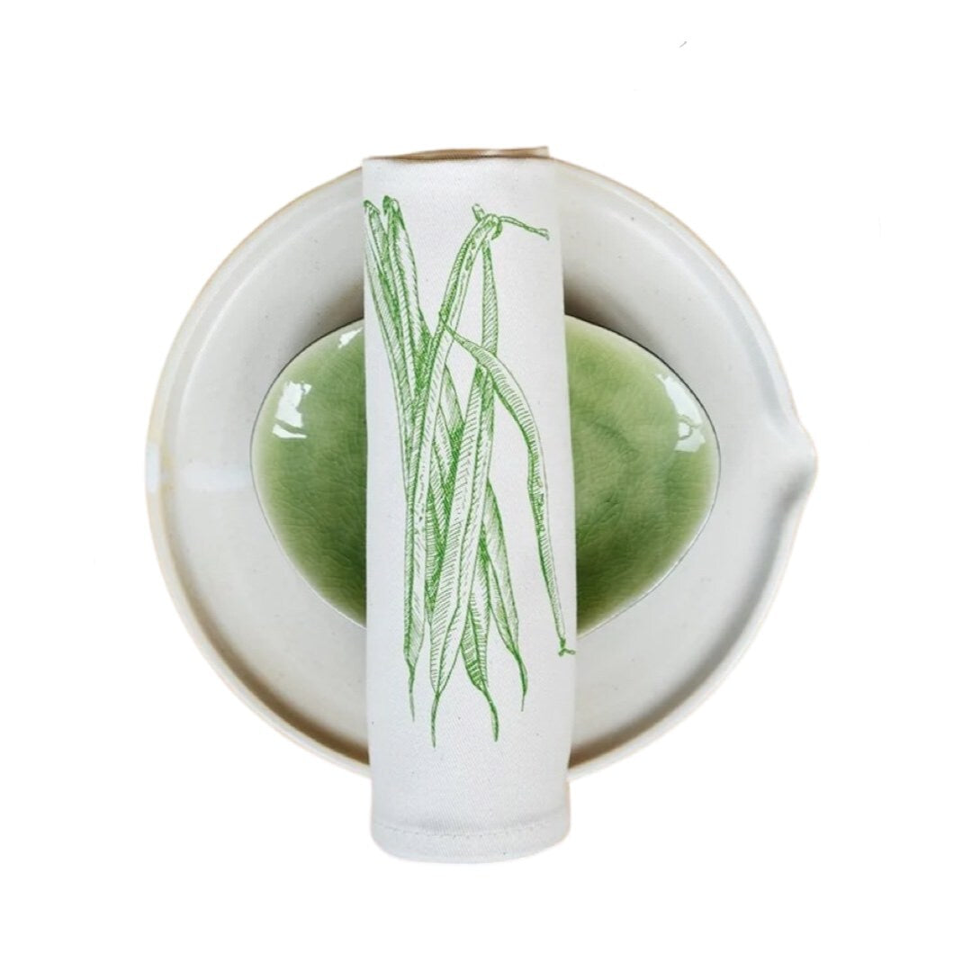 Cream cotton napkin with screen printed green beans rolled on a plate.