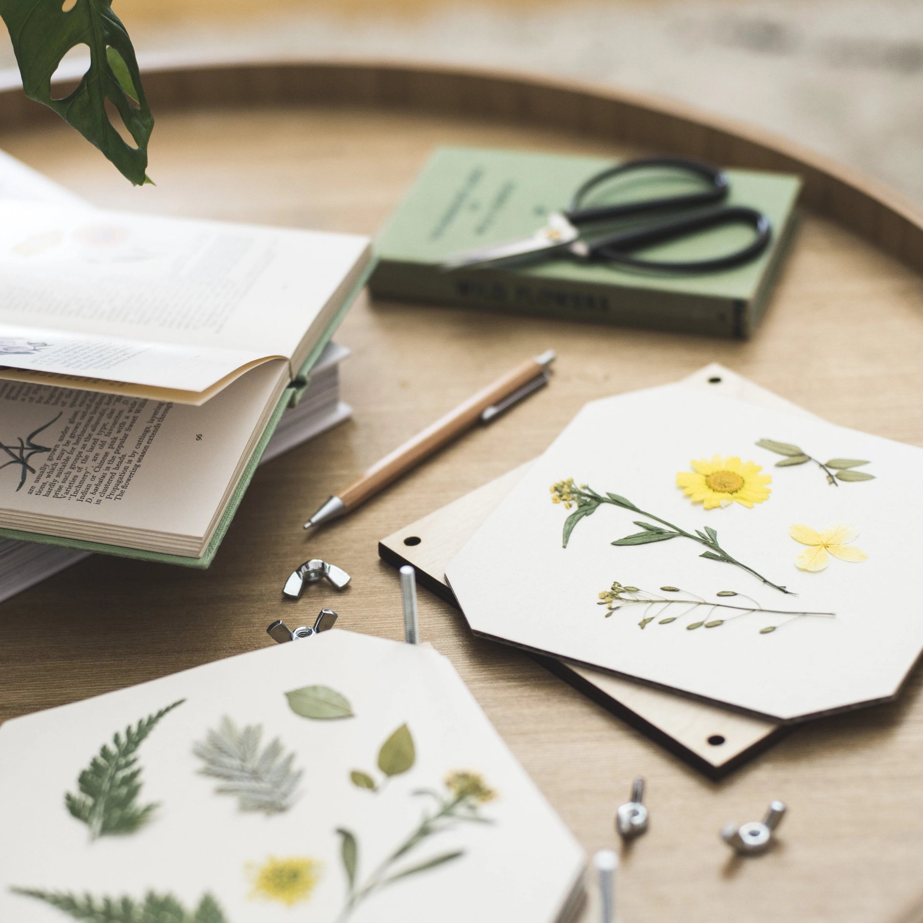 Hexagonal cards with flowers being pressed on a wooden surface with stationery items.