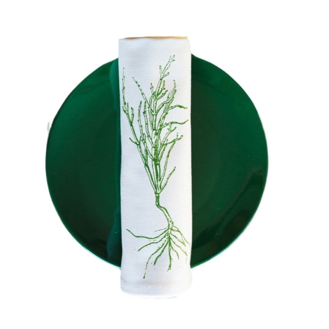 Cream cotton napkin with a green samphire rolled on a plate.