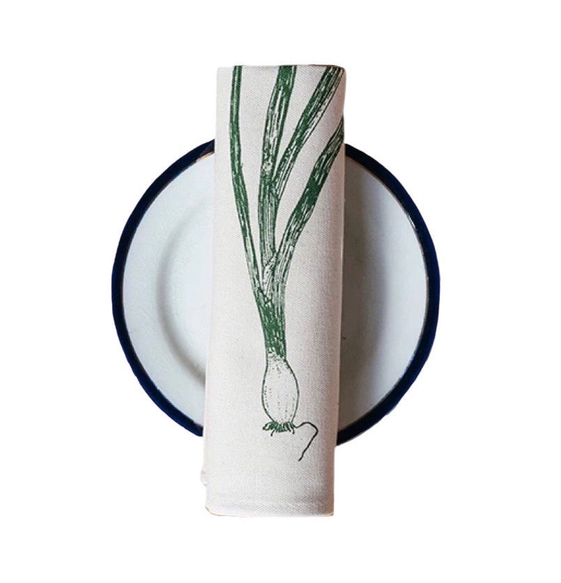 Cream cotton napkin with a green spring onion rolled on a plate.