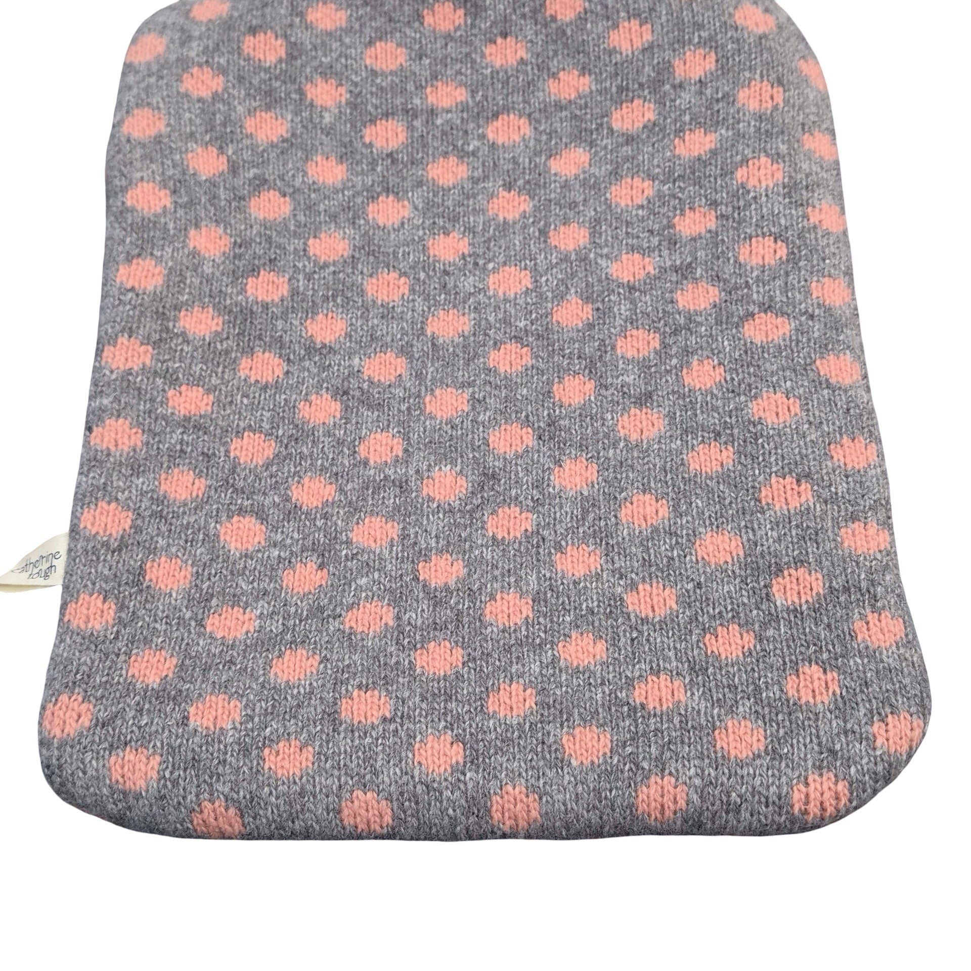 A rectangular grey knit hot water bottle cover with a repeating pattern of dusty pink polka dots, shown against a plain white background.