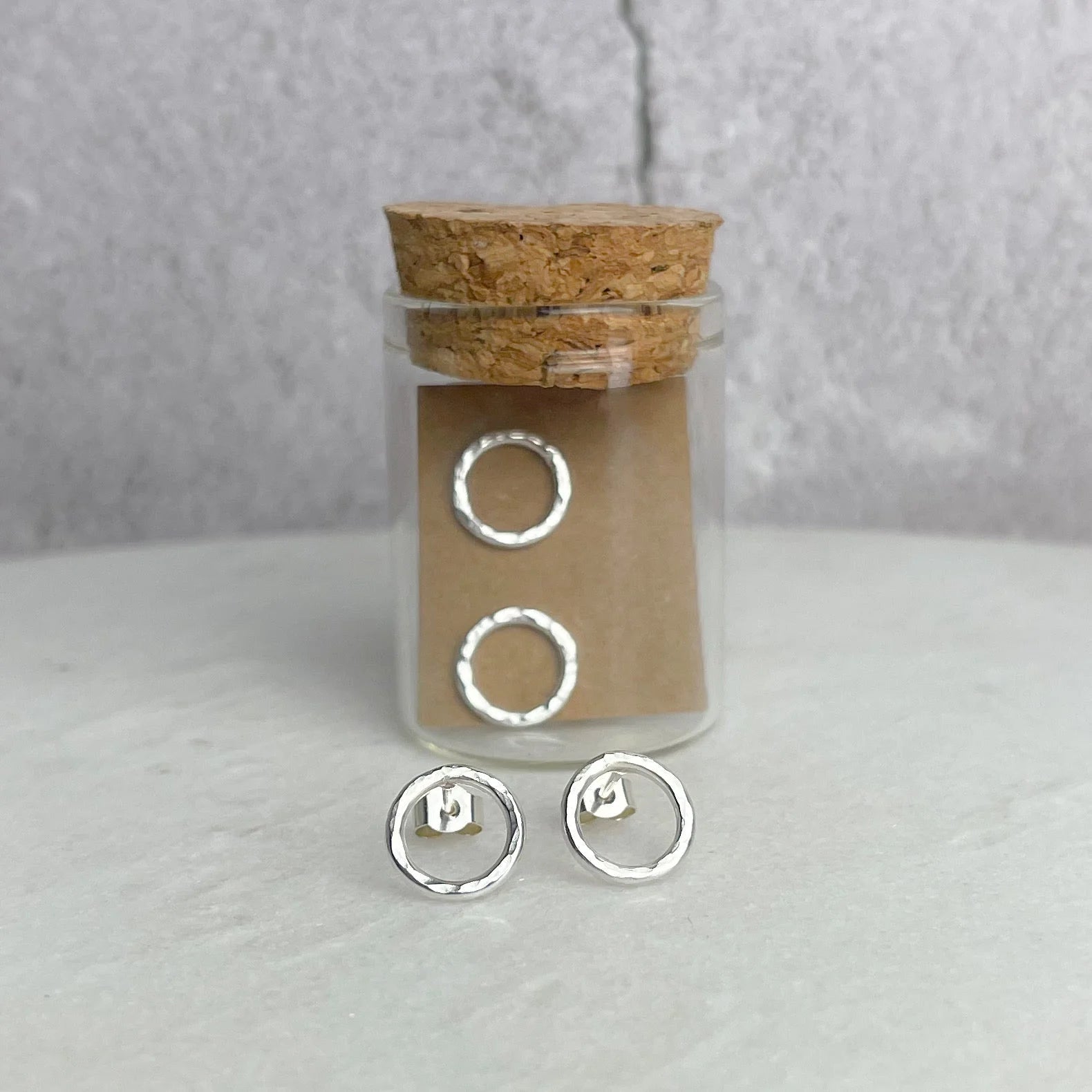Silver hoop earrings in a glass jar with cork lid on a light gray background.