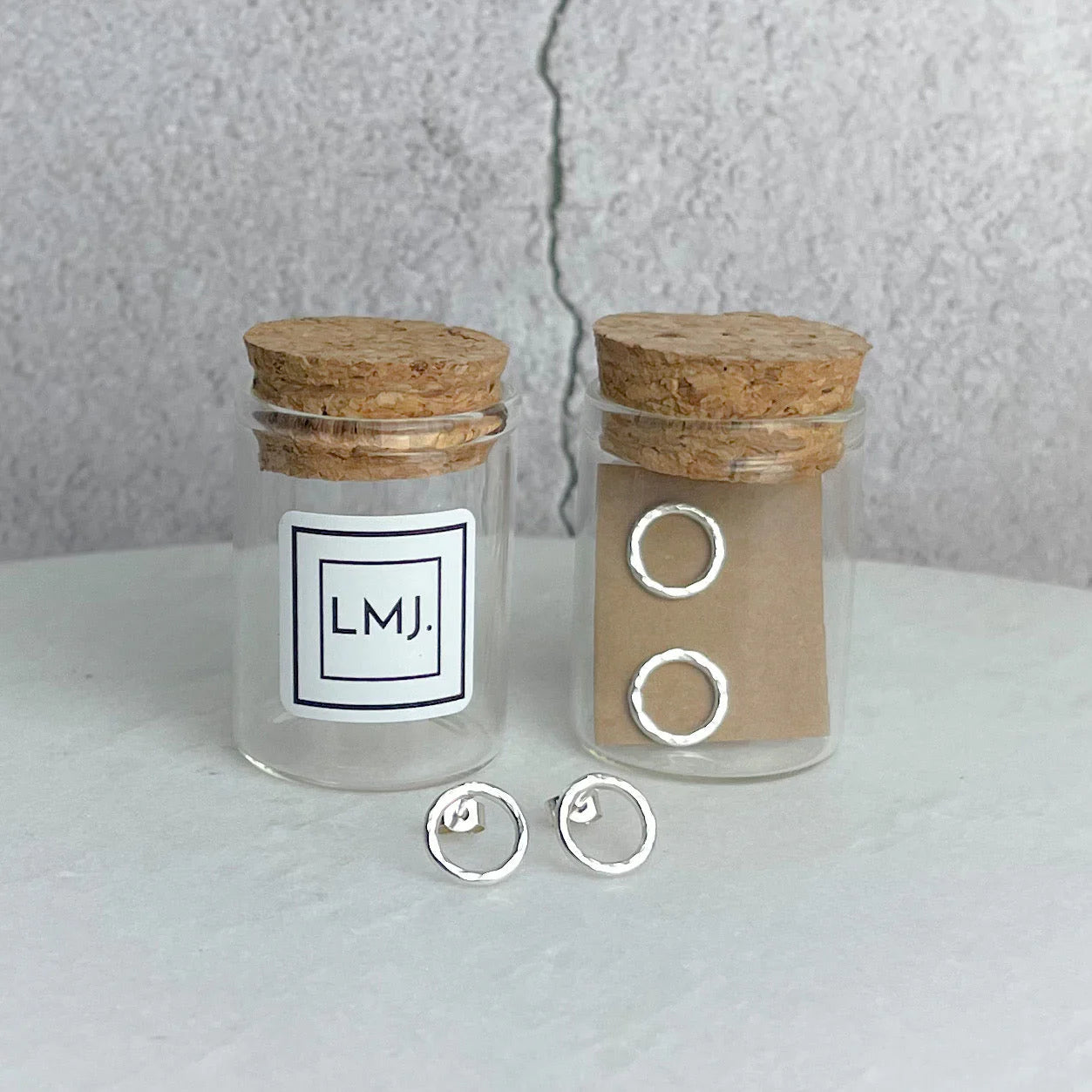 Silver hoop earrings in glass jars with cork lids on a light surface.