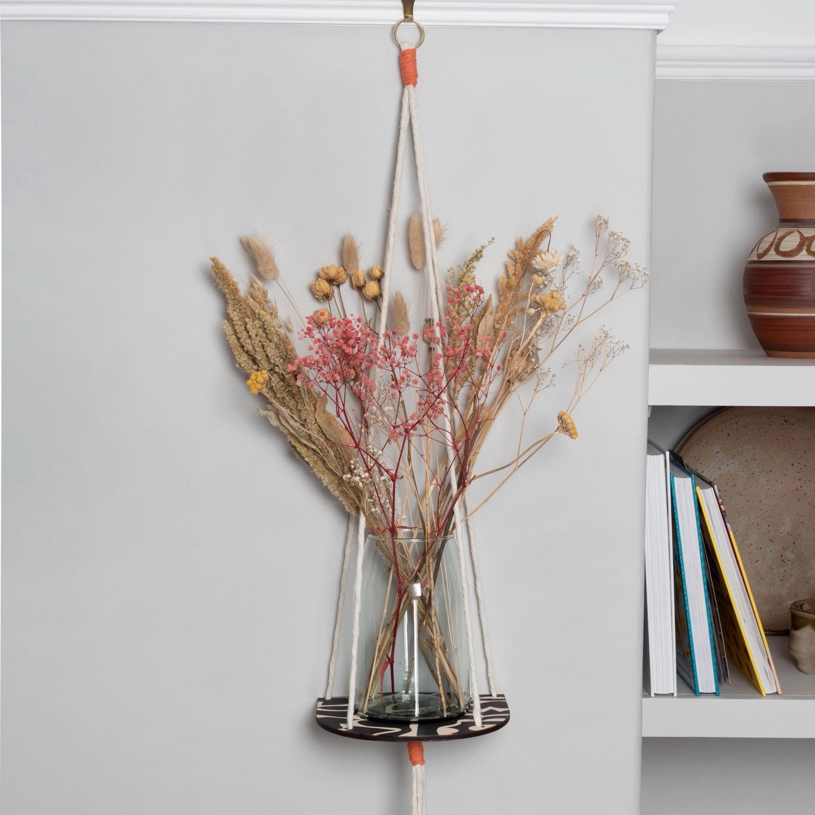 Black hanging plant shelf with dried flowers, being displayed on a wall.