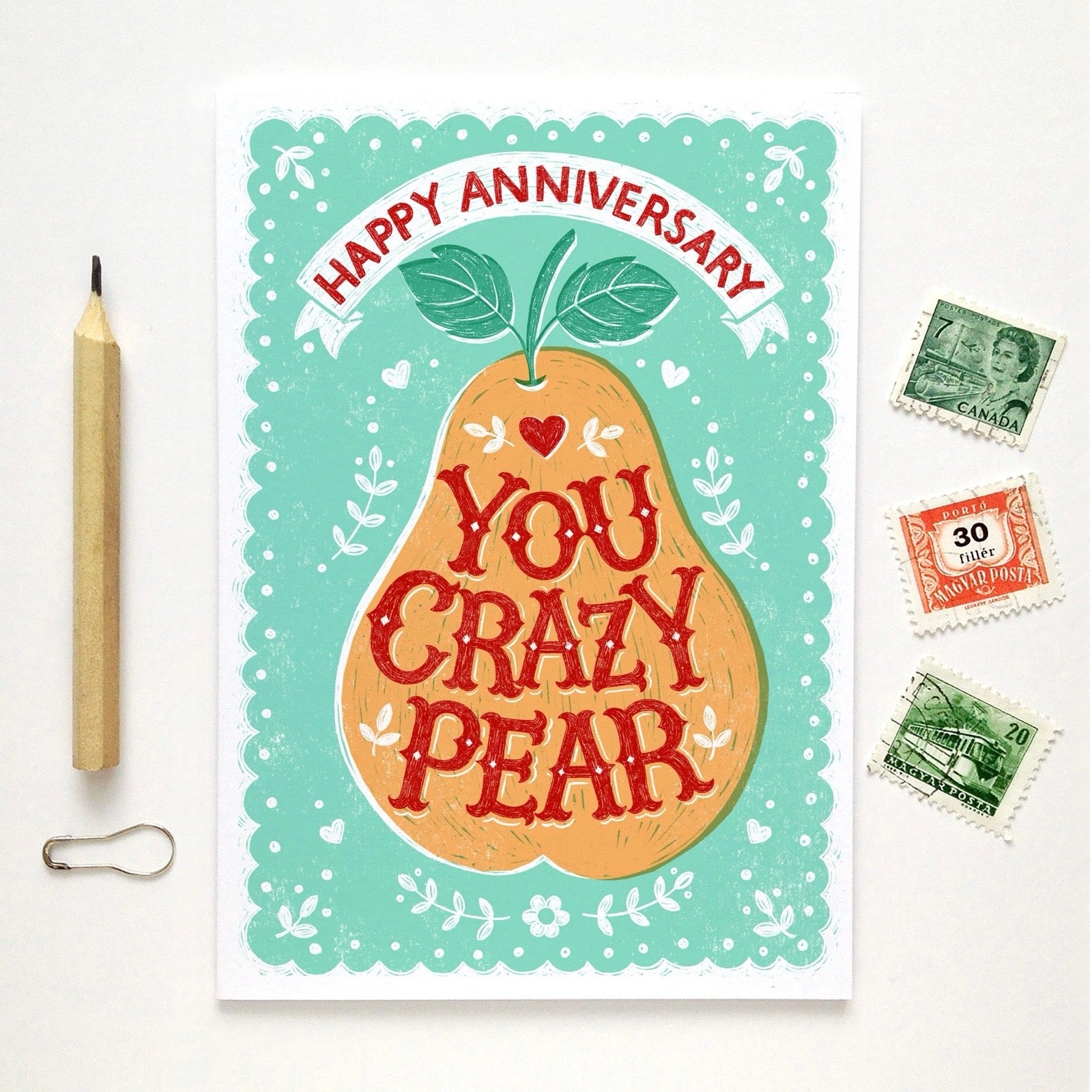 Card with a pear illustration and text 'Happy Anniversary, You Crazy Pear' on a white background with stamps and a pencil.