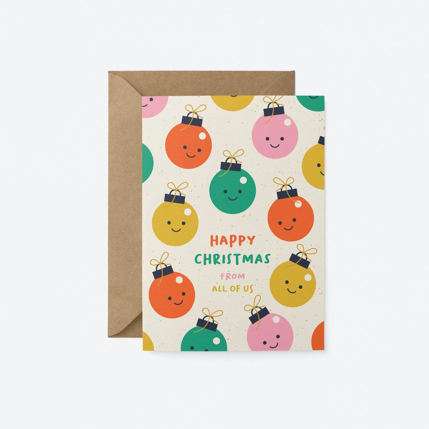 A Christmas greeting card with a kraft envelope behind it, featuring a cream background with colorful smiling ornament illustrations and the text 'Happy Christmas from all of us'.