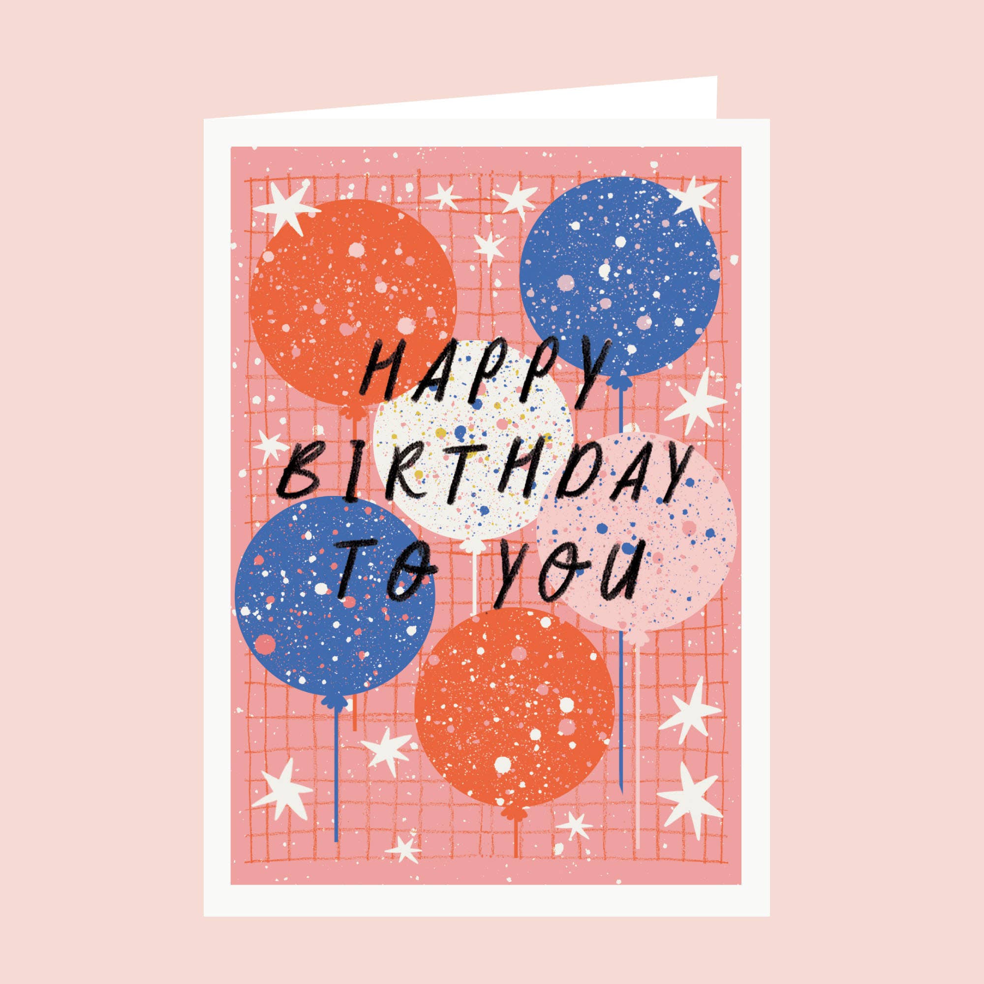A square greeting card with a pink grid background and illustrated balloons in orange, blue, and pale pink, overlaid with the handwritten text 'HAPPY BIRTHDAY TO YOU.' The card is shown slightly open against a soft pink background.