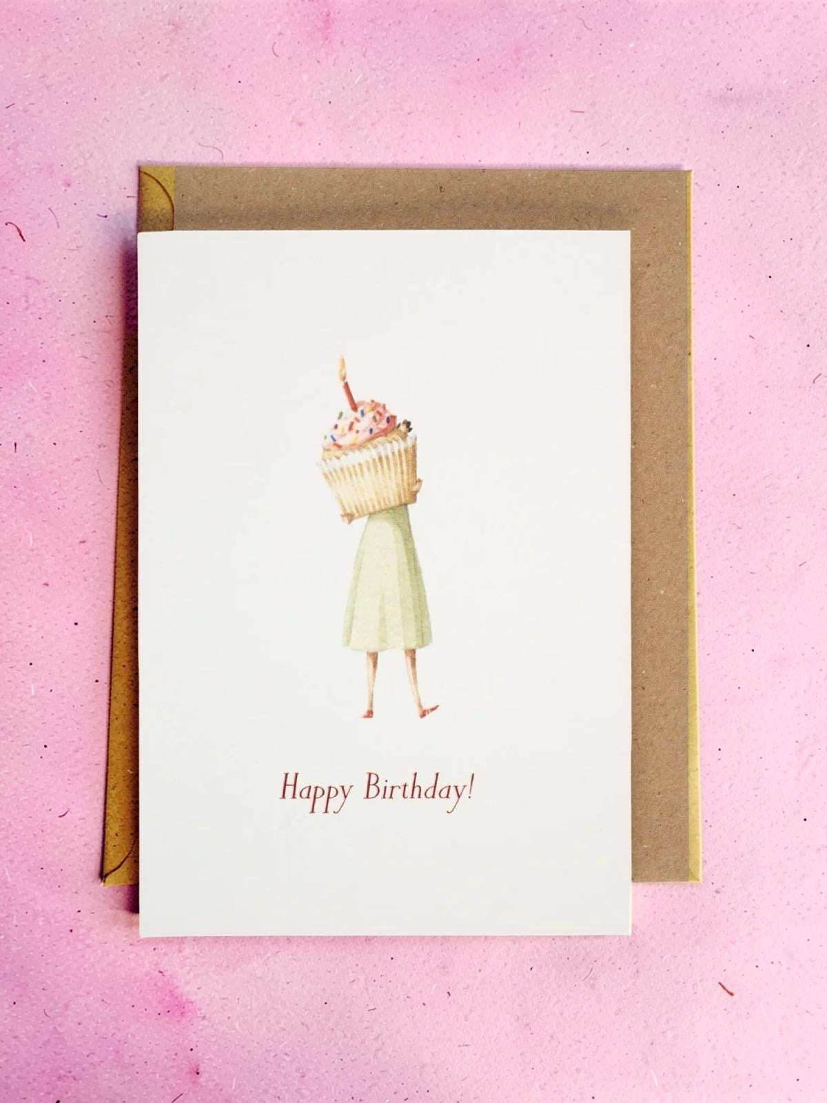 Greeting card with a woman holding a large cupcake and 'Happy Birthday!' text on a pink background.