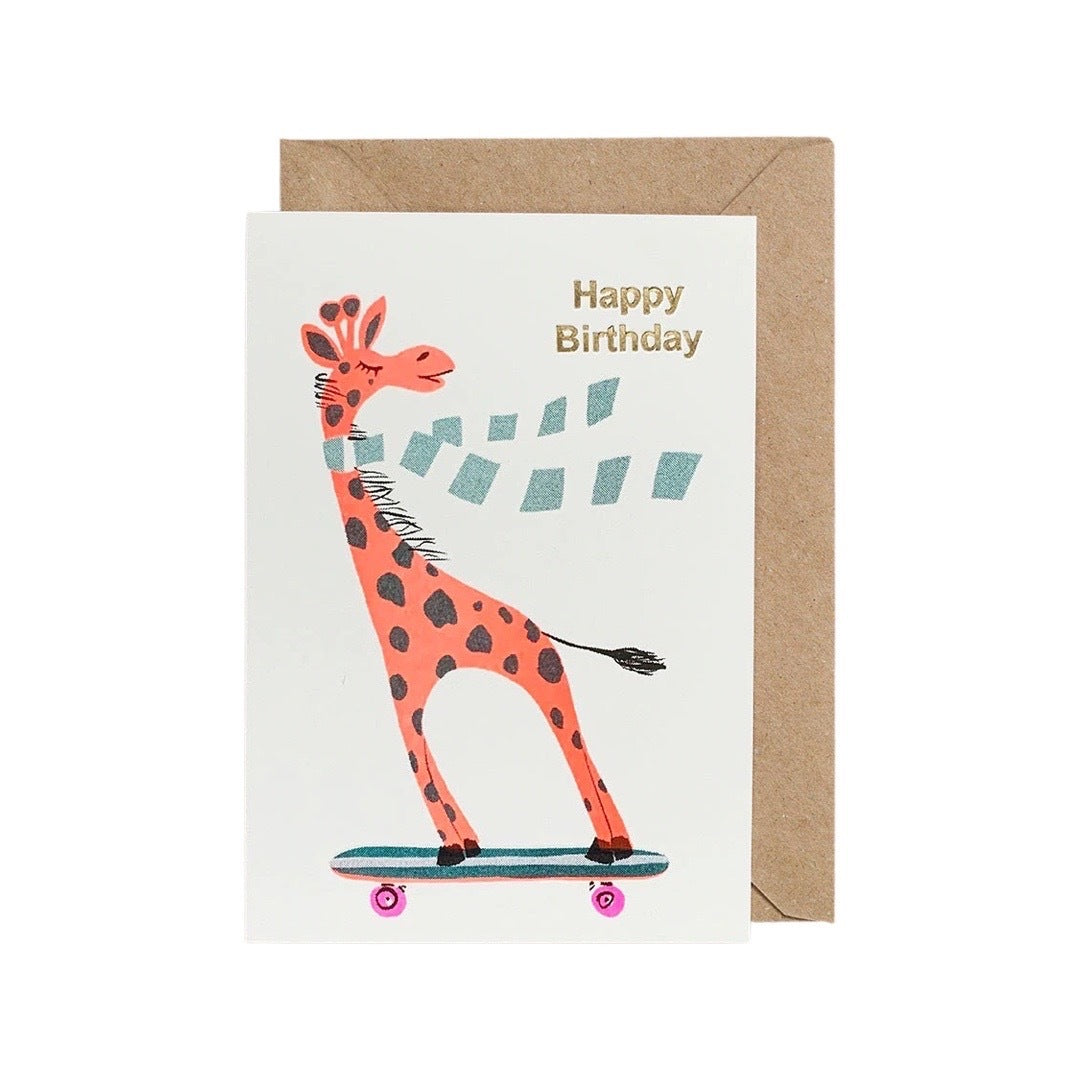 Birthday card featuring a giraffe wearing a blue and white striped scarf riding a skateboard and the text 'Happy Birthday' written in gold.