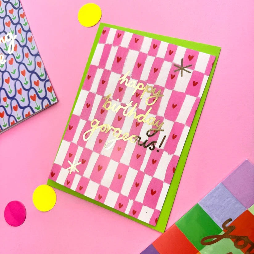 Checkered white and pink card on a pink card with decorative items on the desk.
