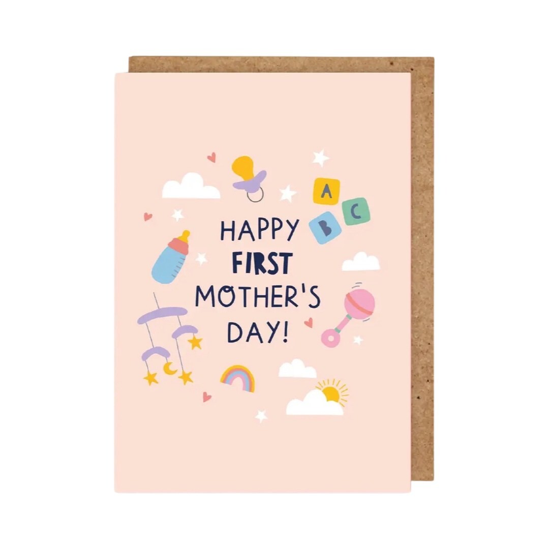 Mother's Day card for a new mum featuring the text 'Happy First Mother's Day' in navy text against a peach background surrounded by a baby rattle, baby bottle, building blocks and other baby-themed illustrations.