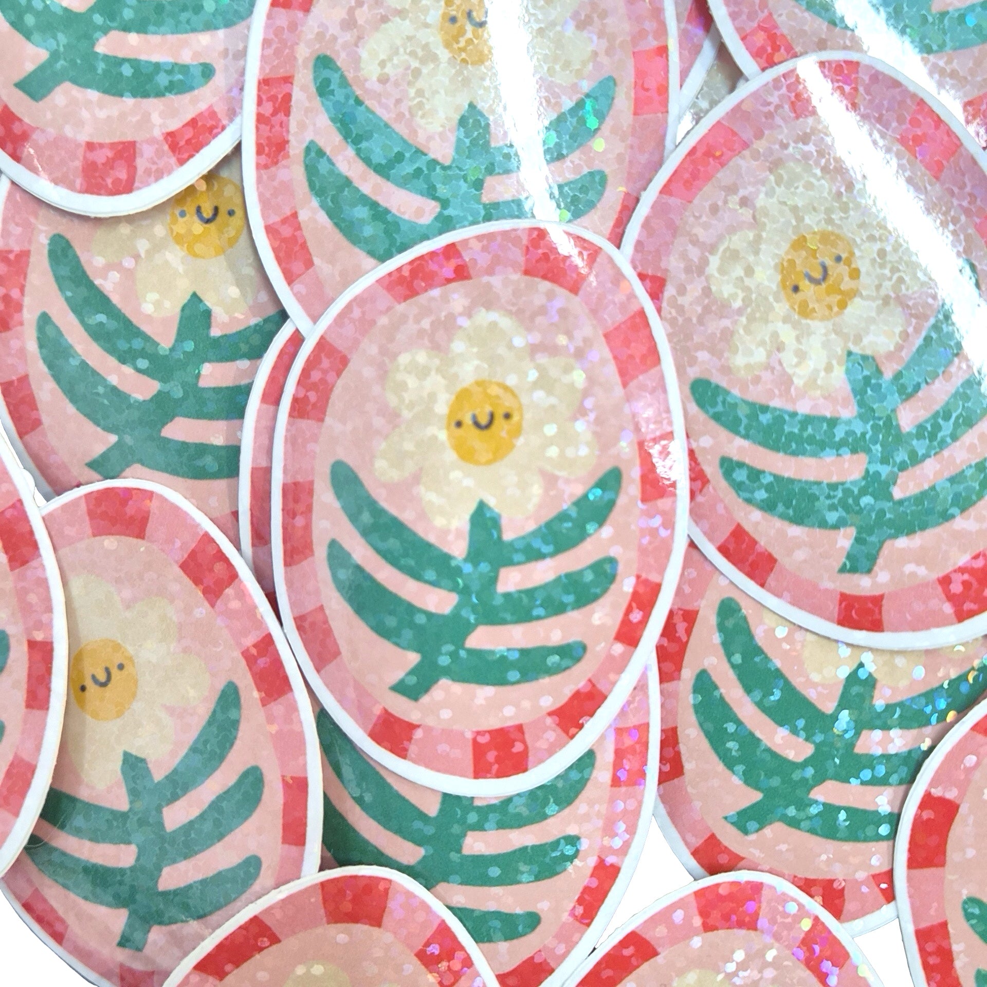 A close-up of multiple oval stickers featuring a cute smiling sunflower design with green leaves, a yellow face, and a pink striped border on a glittery background.