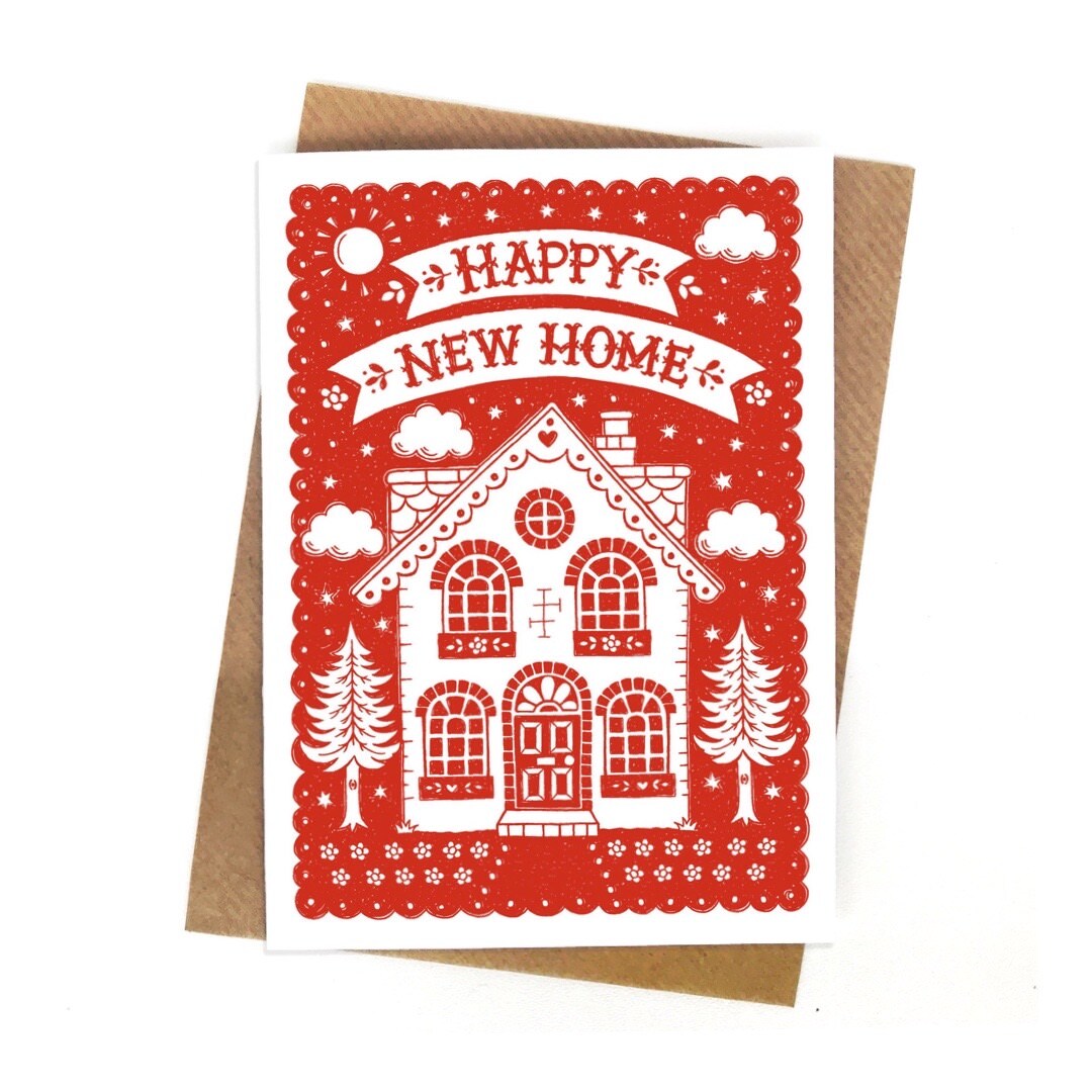 A red card with a white two storey house with a chimney and a fir tree on either side. The text 'Happy New Home' is written in red inside a white banner above.