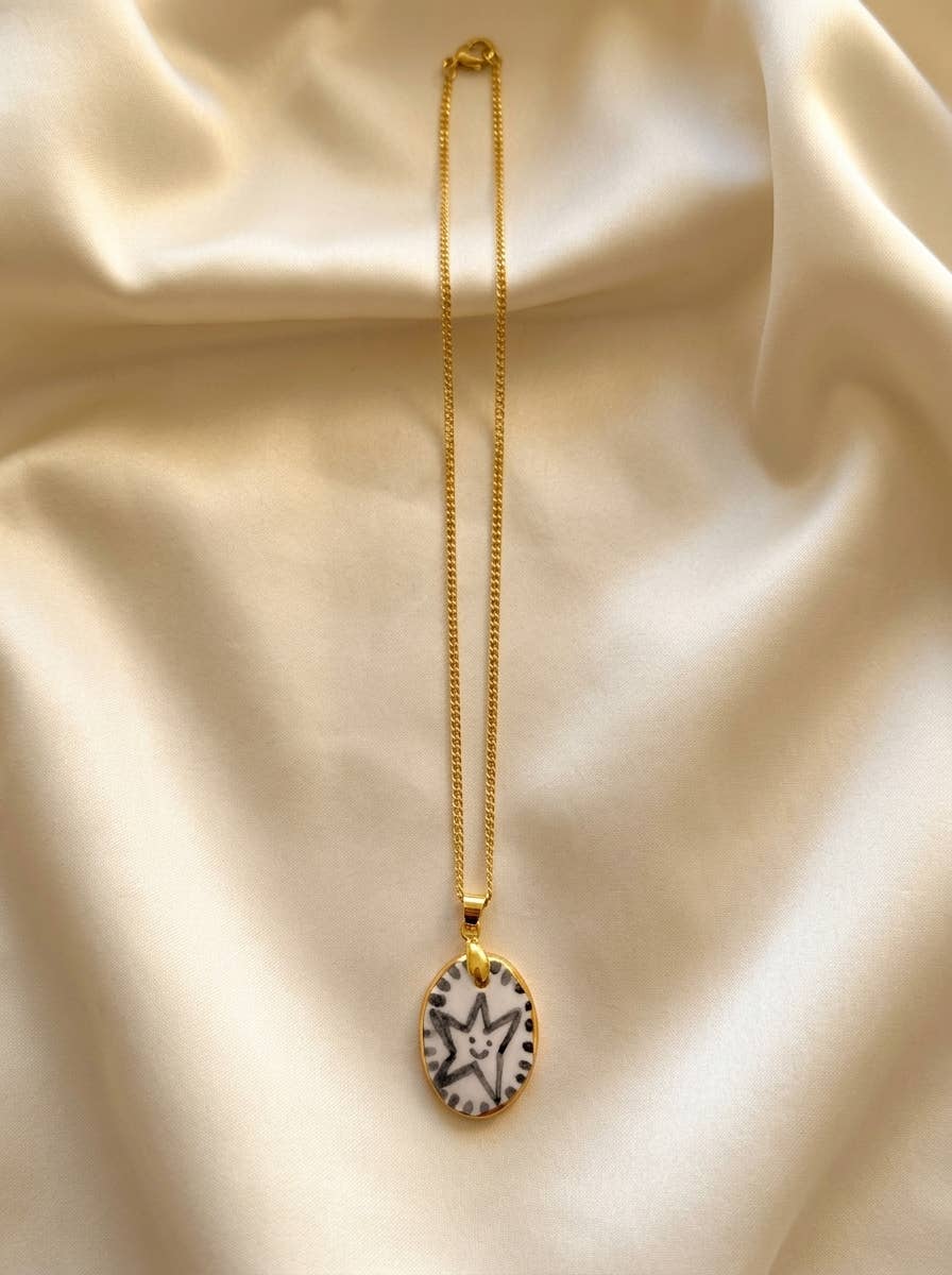 Gold necklace with a black and white pendant on a beige fabric background.
