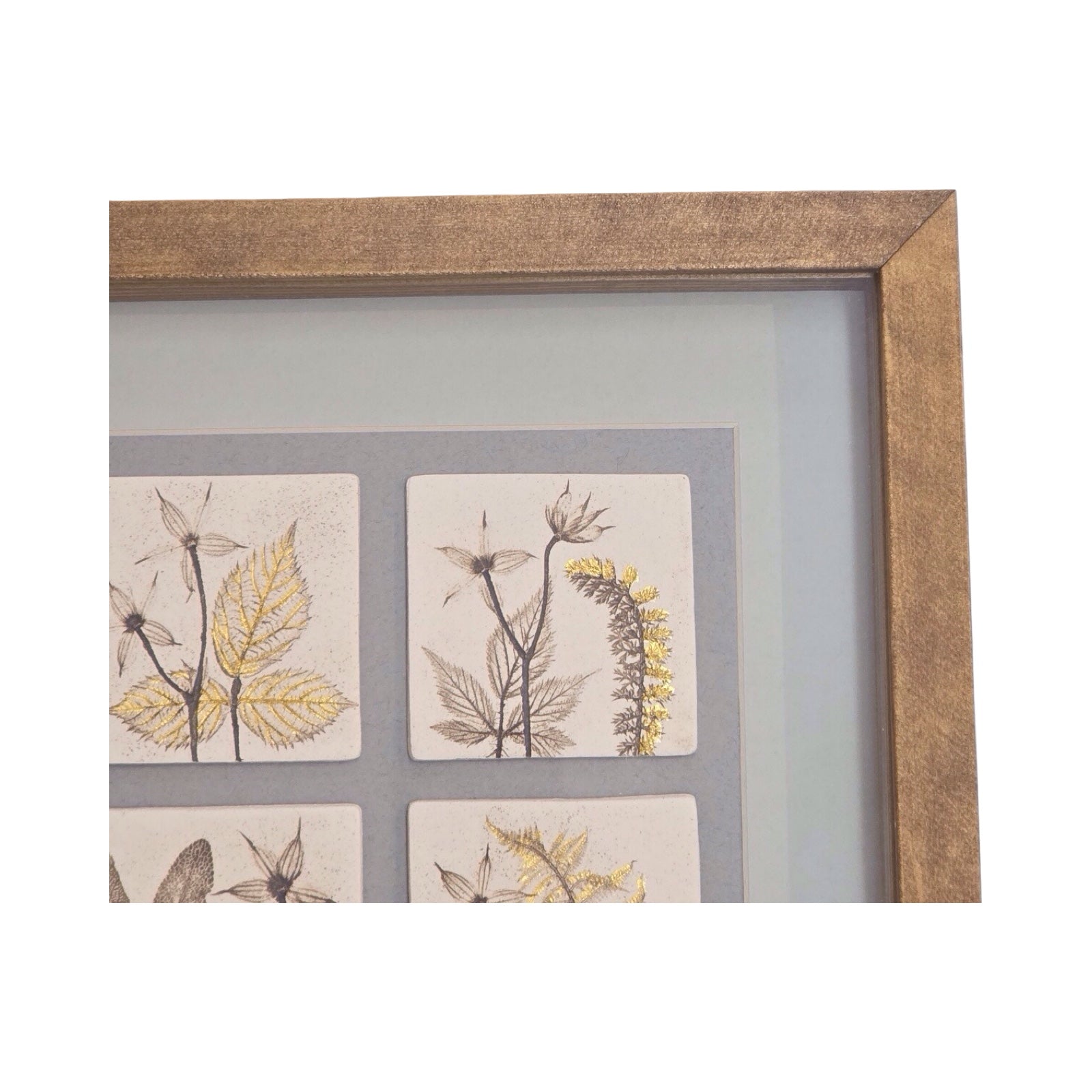Framed artwork with botanical tiles on a grey background in oak frame with gold leaf detailing. 