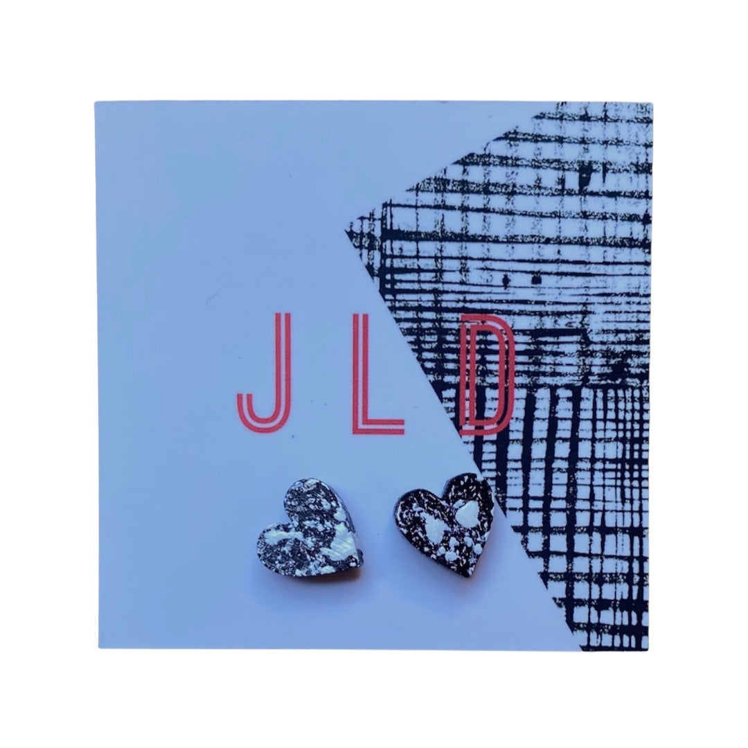 A pair of heart-shaped stud earrings with a black and white splash design, made of silver plating and painted wood.