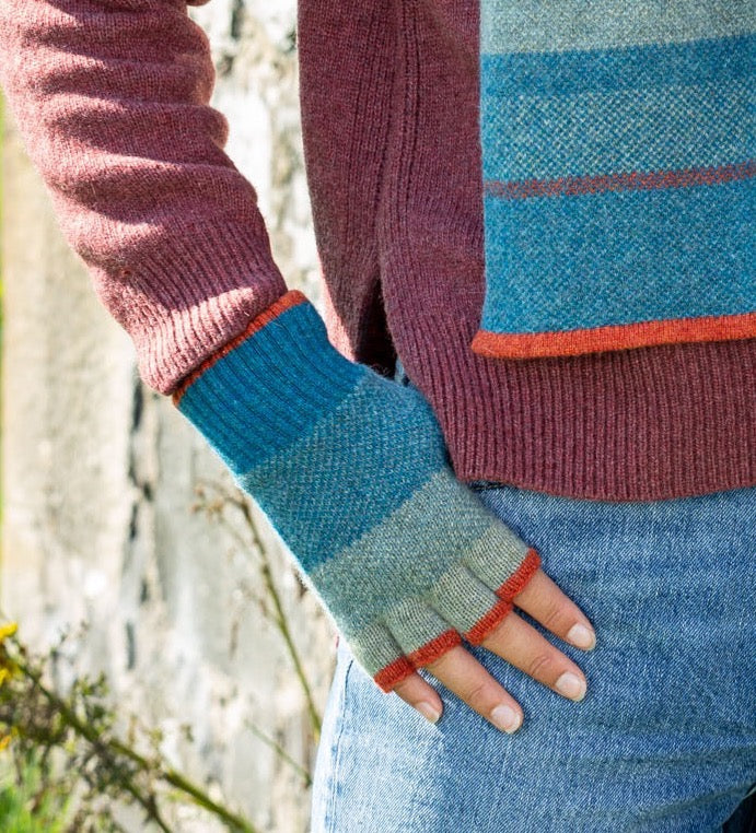 Person wearing colourful knitted gloves with a blurred natural background.