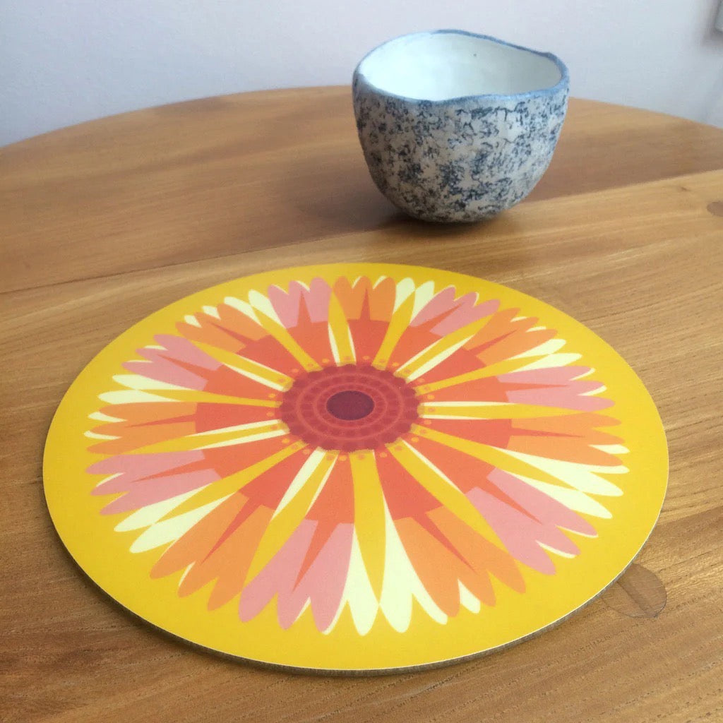 Round colourful placemat with a floral design on a wooden table.