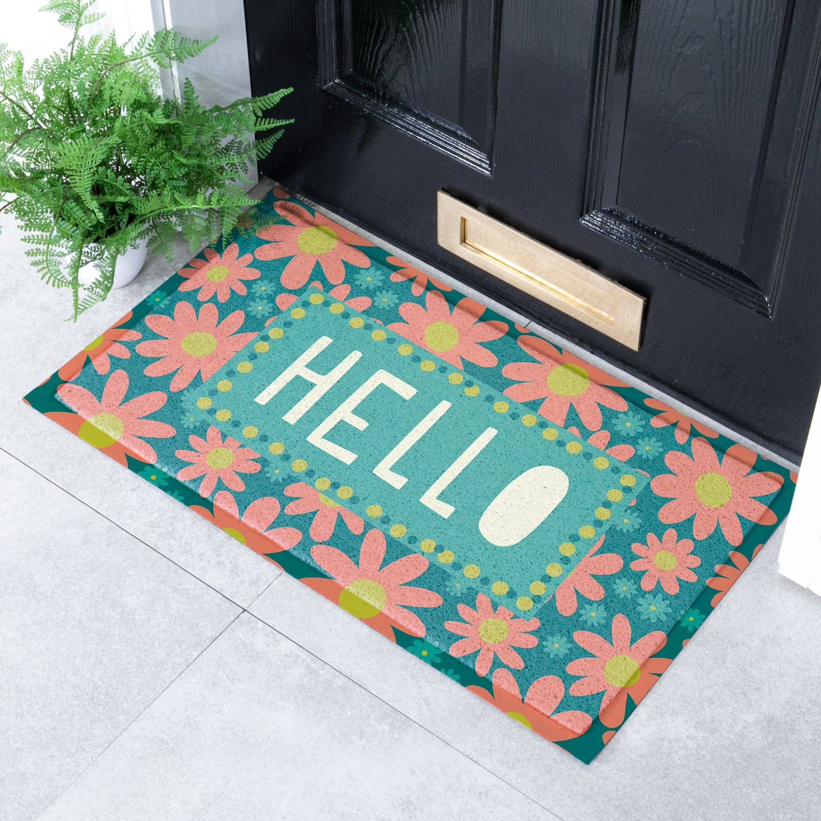 A rectangular doormat with a retro daisy pattern and the word 'HELLO' in the center, placed in front of a black front door on a light gray tiled floor next to a potted fern.