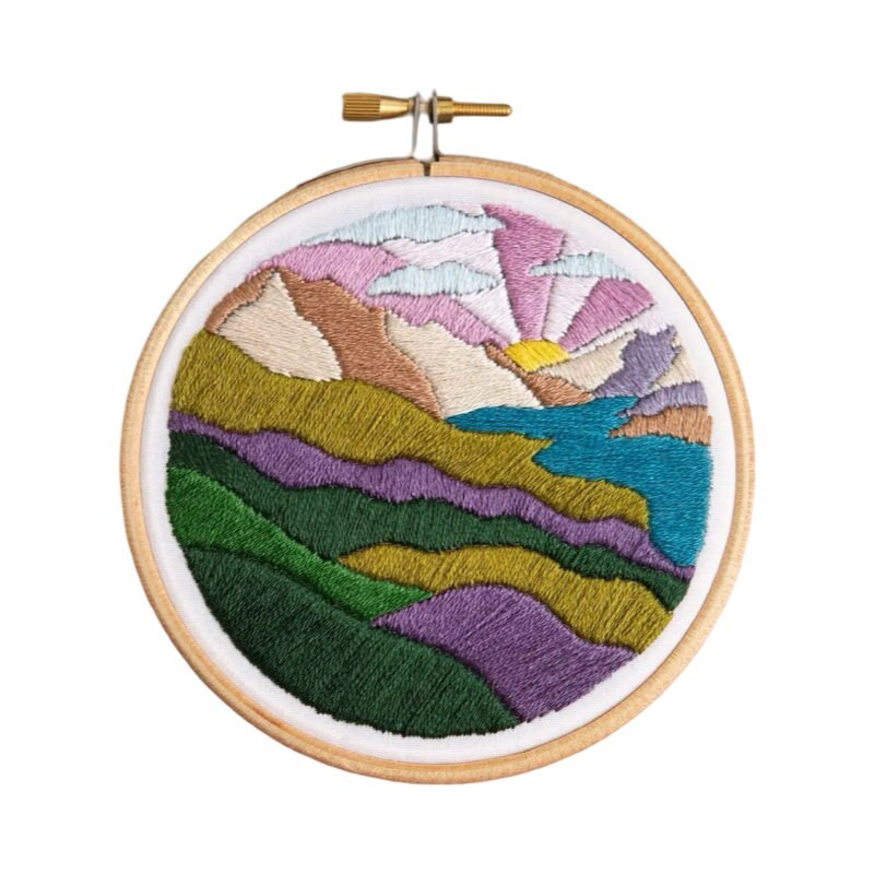 This craft kit teaches you to embroider a highland hills scene in greens and purples, with a purple and pink rising sun.
