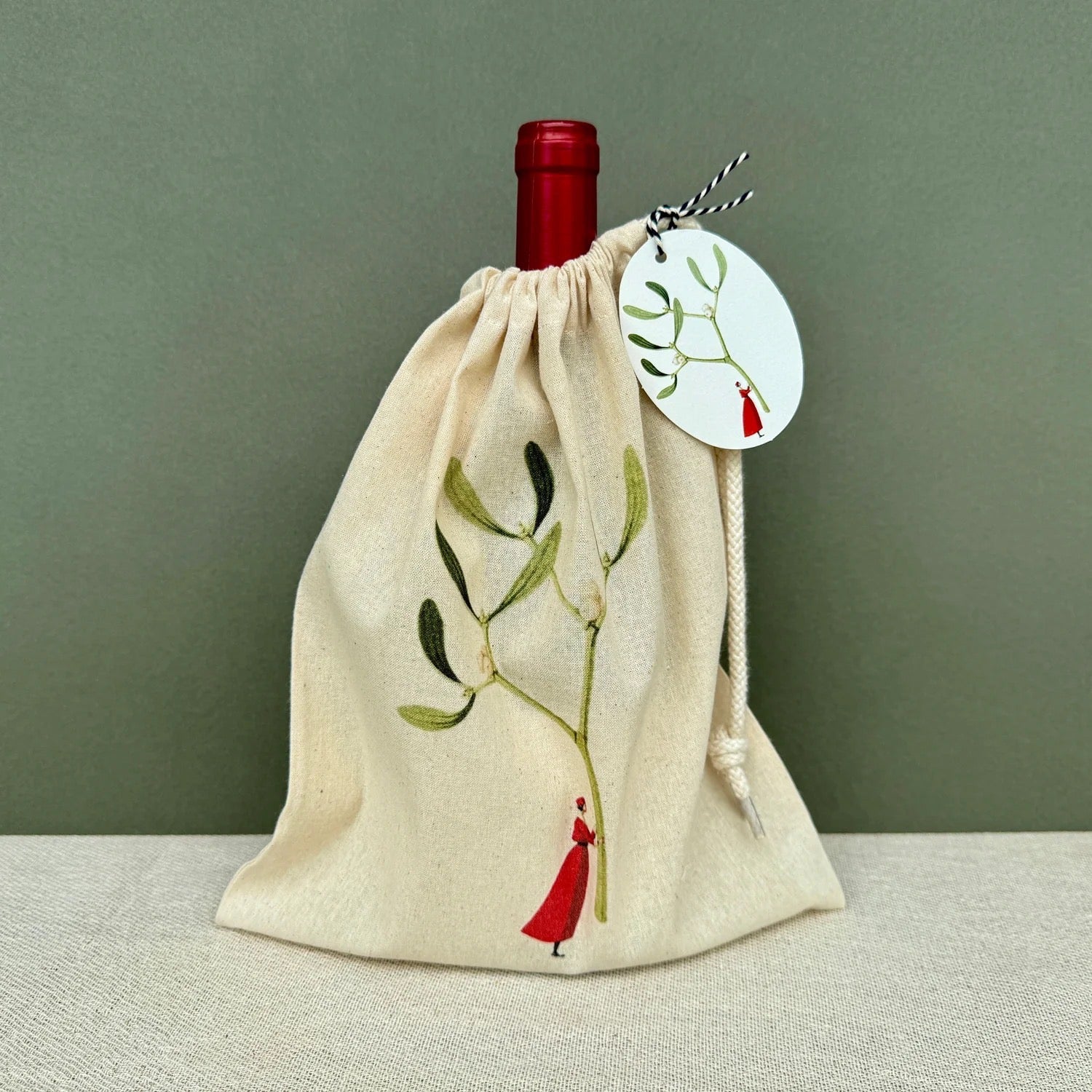 Wine bottle in a decorative cloth bag with a tag on a plain background.