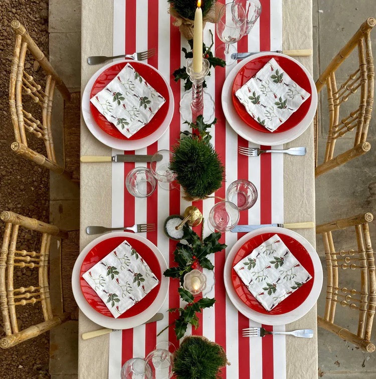Dining table set with red and white striped tablecloth, red plates, and greenery.