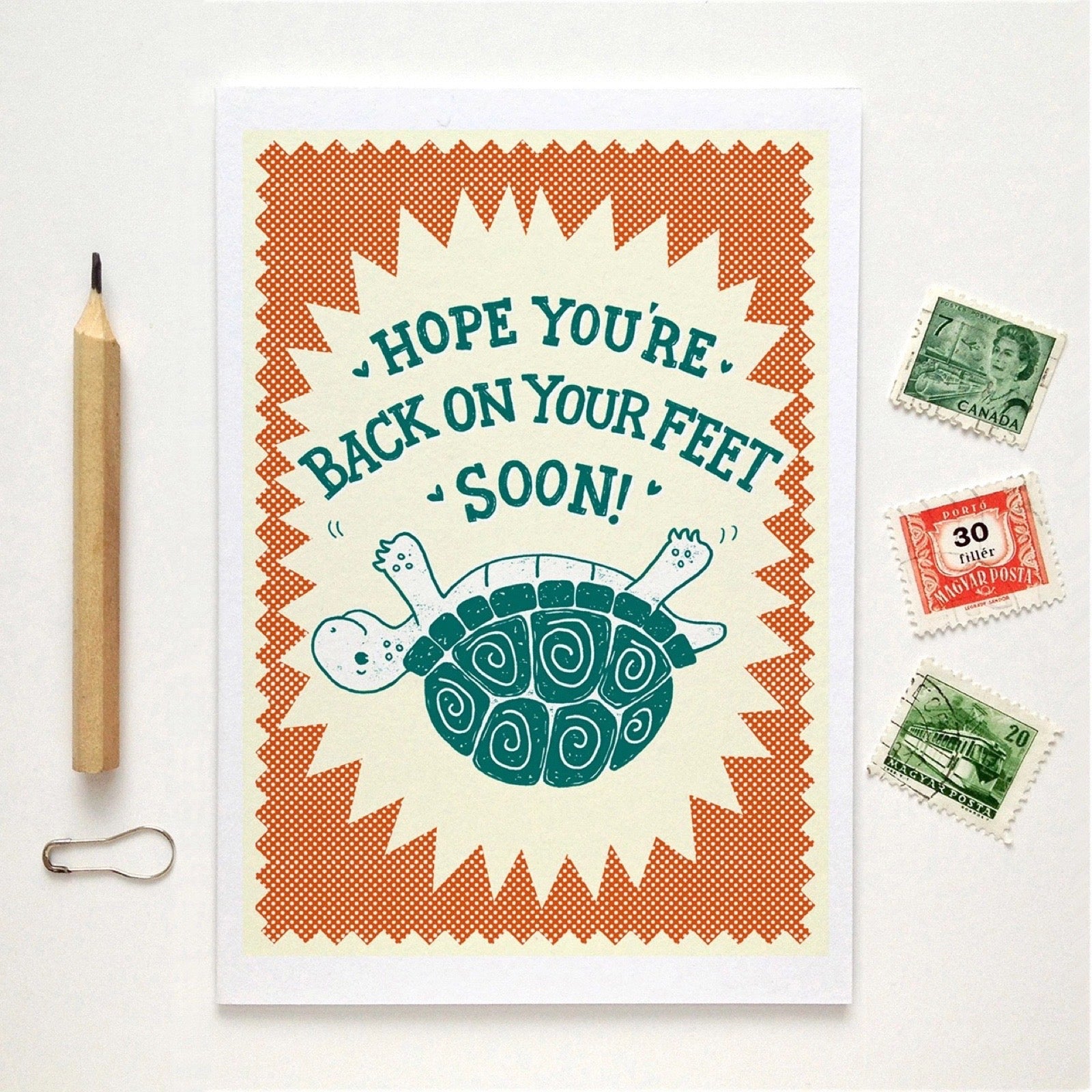 Greeting card with turtle illustration and text 'Hope you're back on your feet soon!' on a white background with stamps and a pencil.