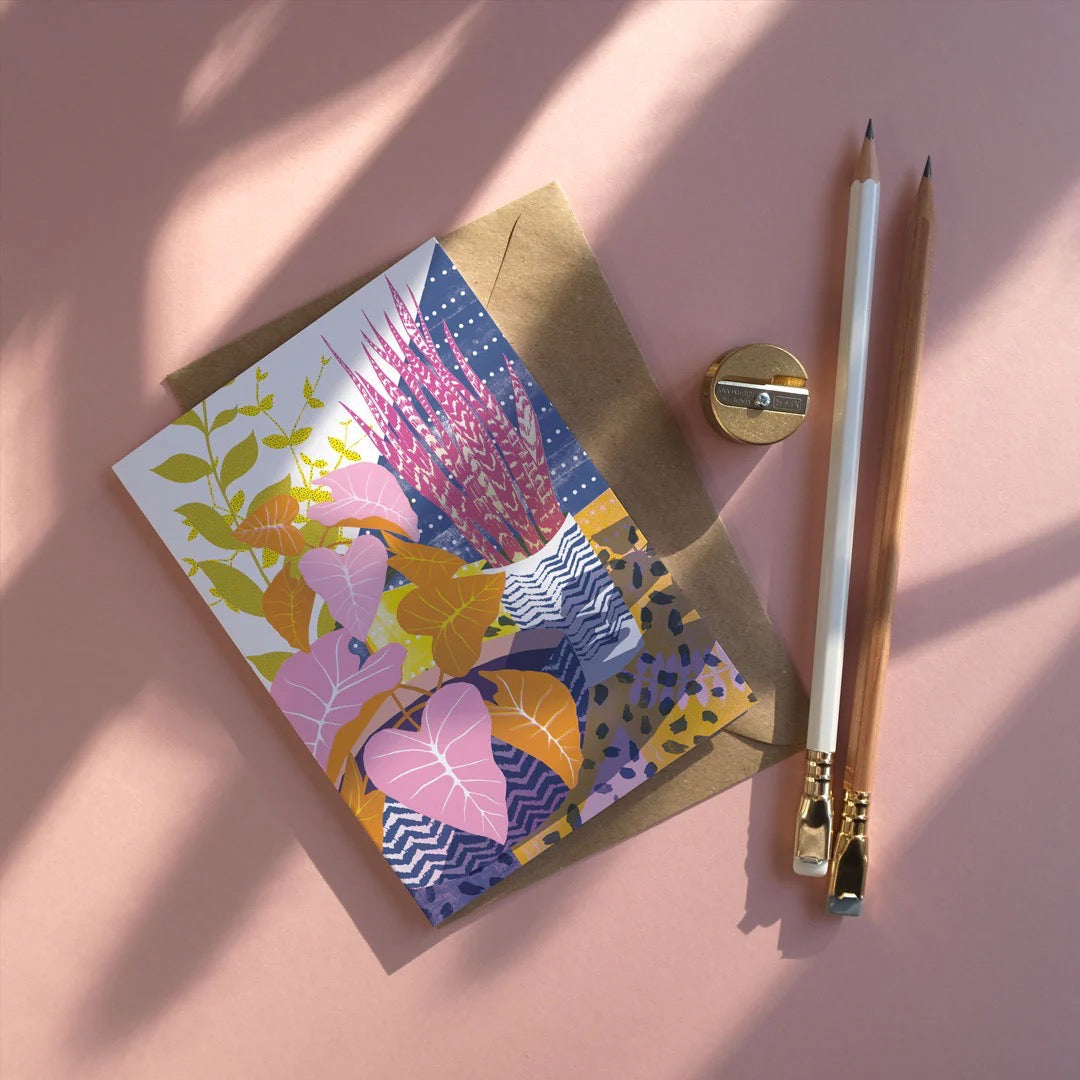Colourful floral card on a pink background with an envelope and pencils.
