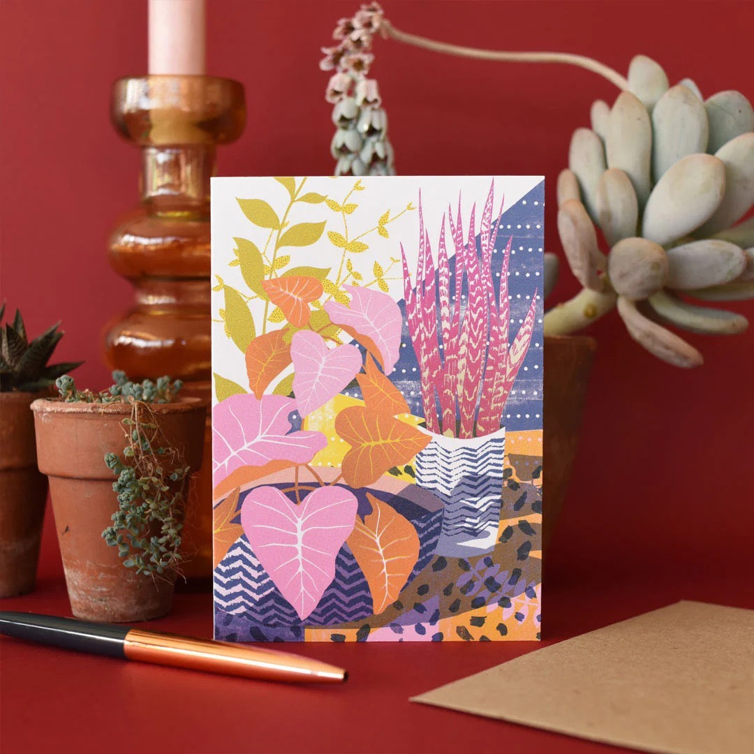 Colourful floral card on a red surface with plants and a pen.