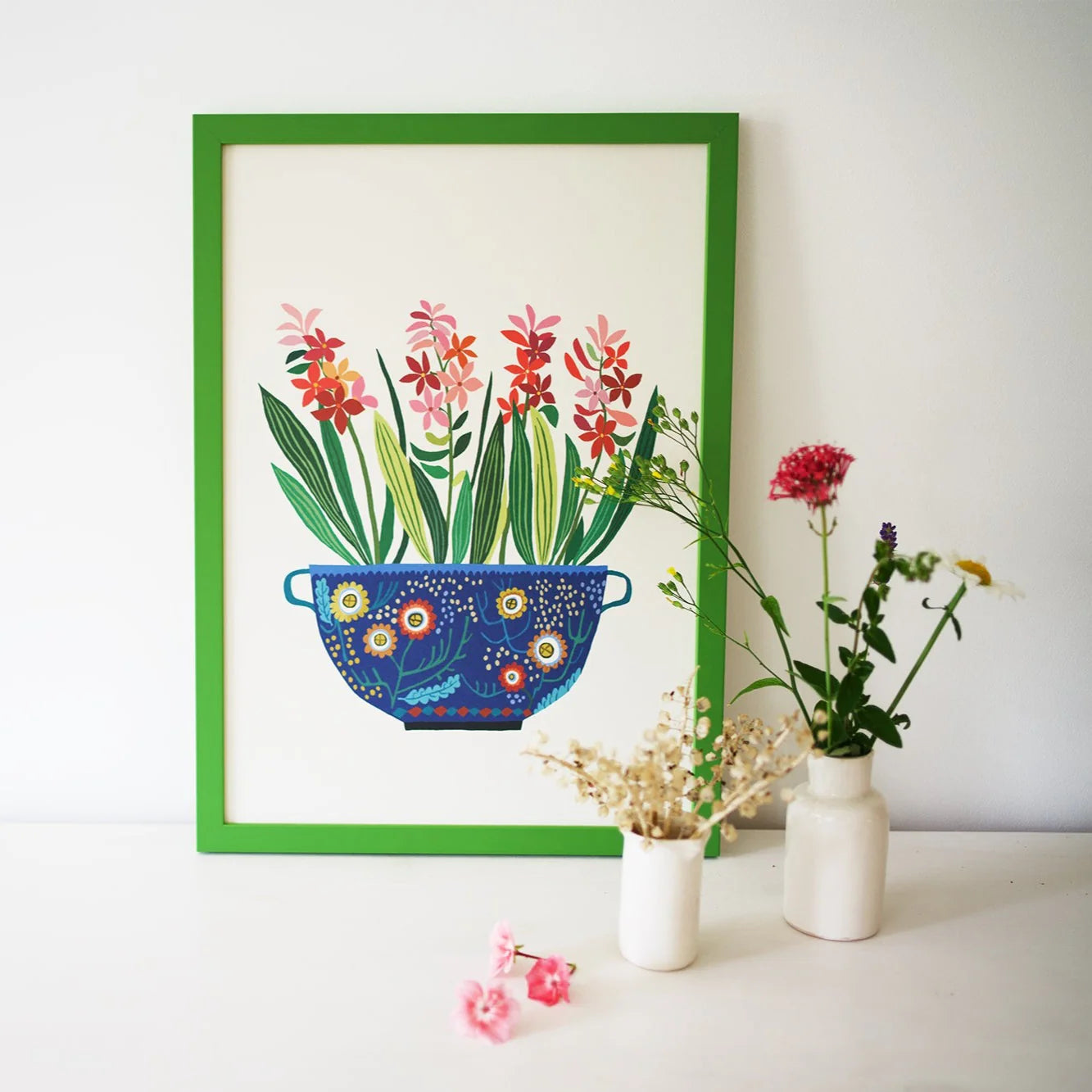 Framed artwork of a colourful flower pot with plants on a white wall.