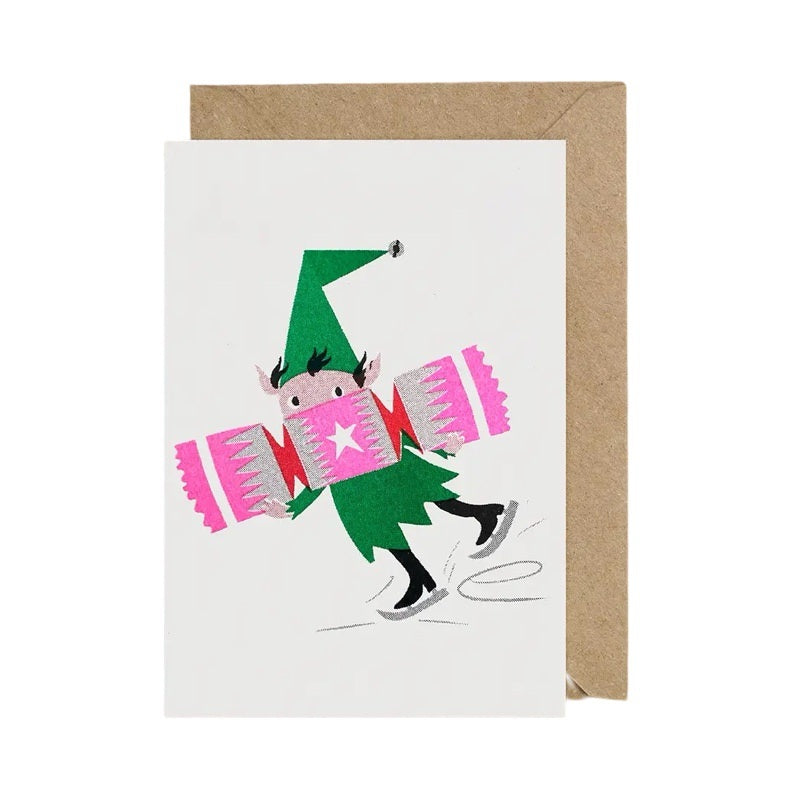 Christmas card featuring an elf ice skating holding a giant pink Christmas cracker.