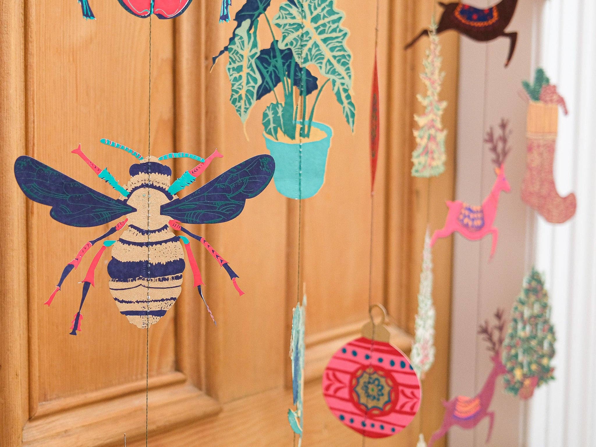 Decorative string art with colourful insects and plants on a wooden surface.