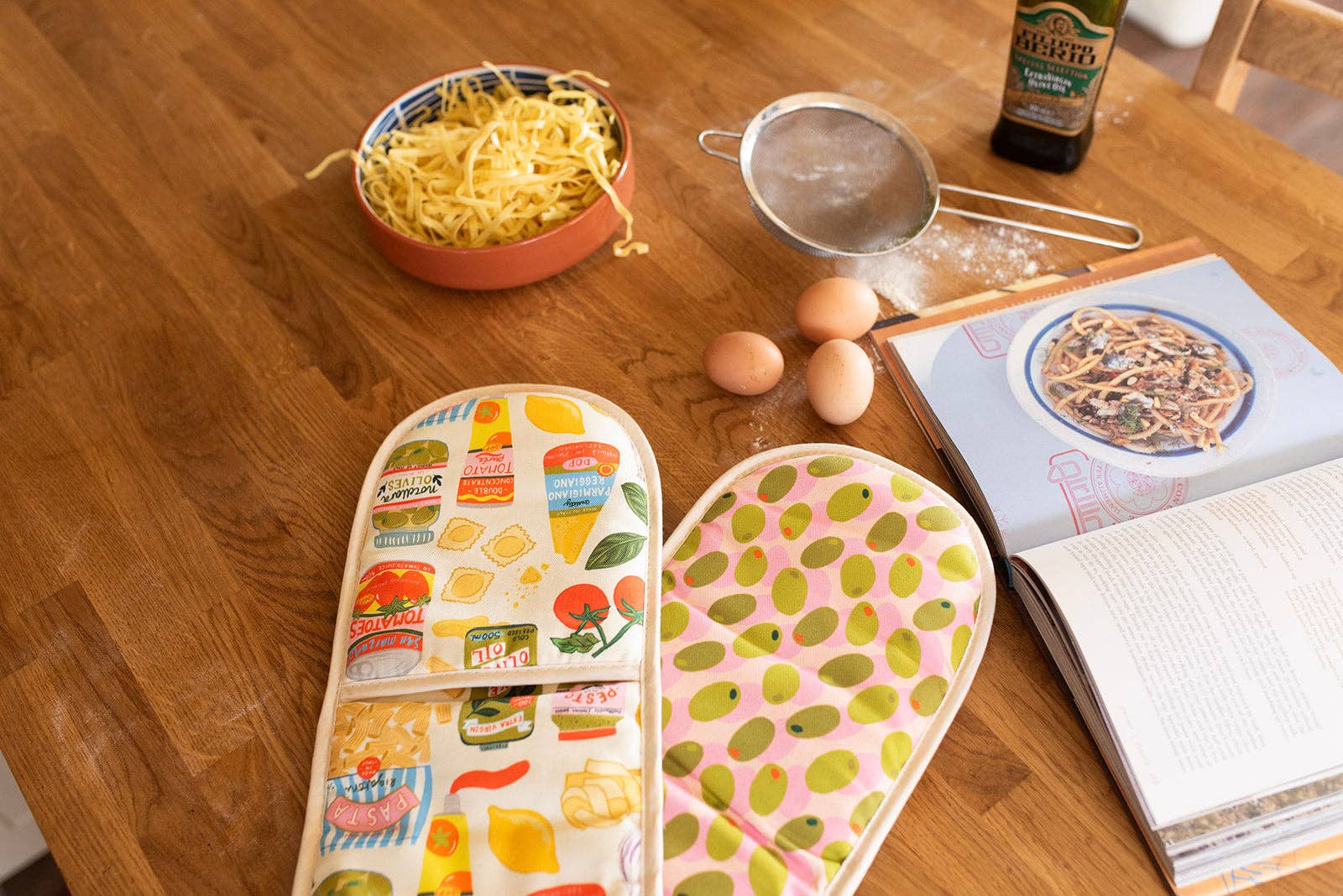Colourful kitchen towels on a wooden table with ingredients and a cookbook.