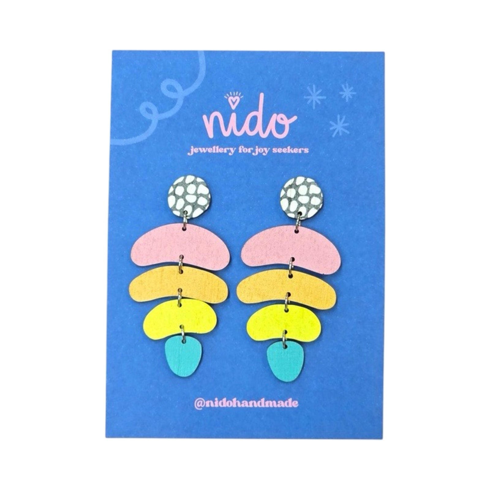 These wooden jellybean earrings feature a black and white pebble effect circular stud with pink, orange, yellow and teal jellybean shapes hanging underneath, presented on a branded blue backing card.