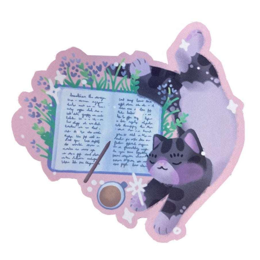 Handmade sticker of a grey and white tabby cat, stretching out over an open journal. With lavender and grass details, a pencil and cup of tea.
