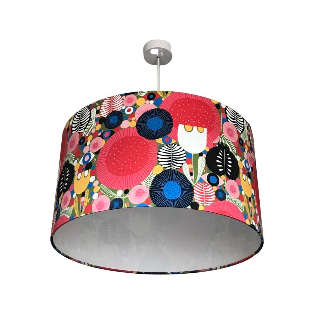 Drum lampshade covered in cotton sateen mid-century inspired fabric with various flowers and leaves in reds, white, yellow, red, pinks, greens and blues.